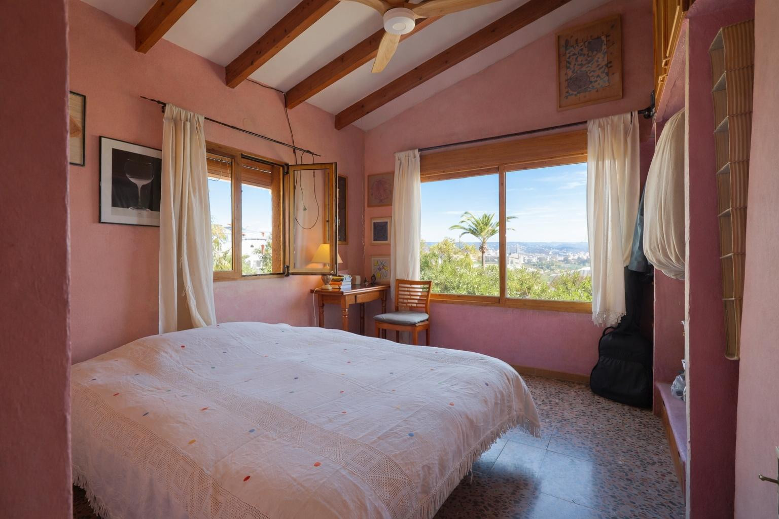 Slaapkamer met houten balkenplafond, warme muurtinten en grote ramen met vrij uitzicht op het mediterrane landschap van Jávea.