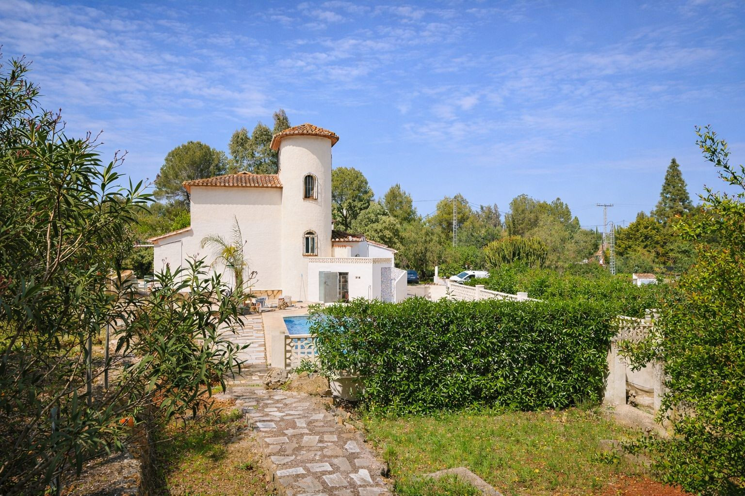 Buitenaanzicht van de villa met ronde toren, terracotta dakpannen en mediterrane tuin met stenen paden en een privézwembad.