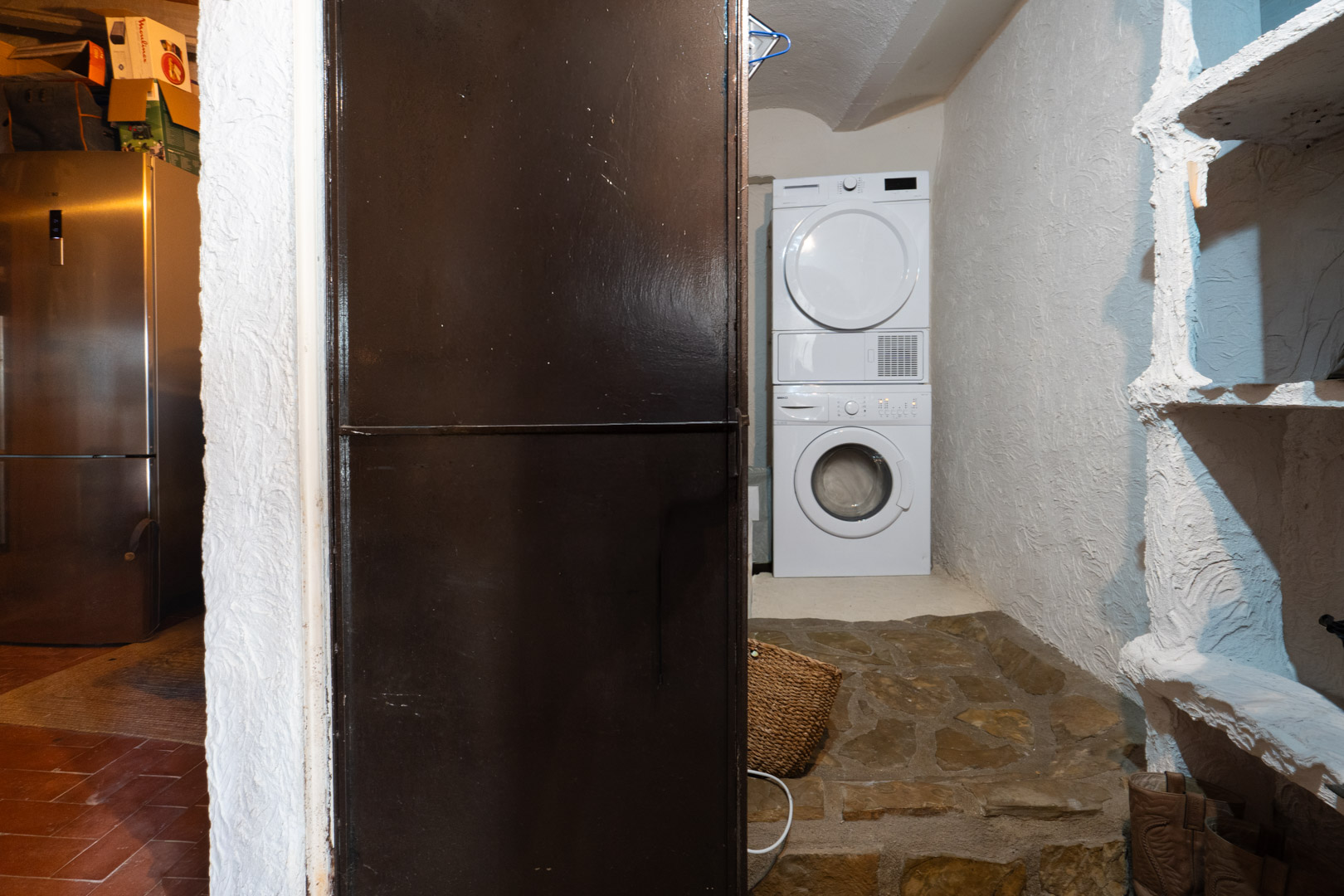 Functionele wasruimte met een gestapelde wasmachine en droger, muren met textuur en een authentieke natuurstenen vloer.
