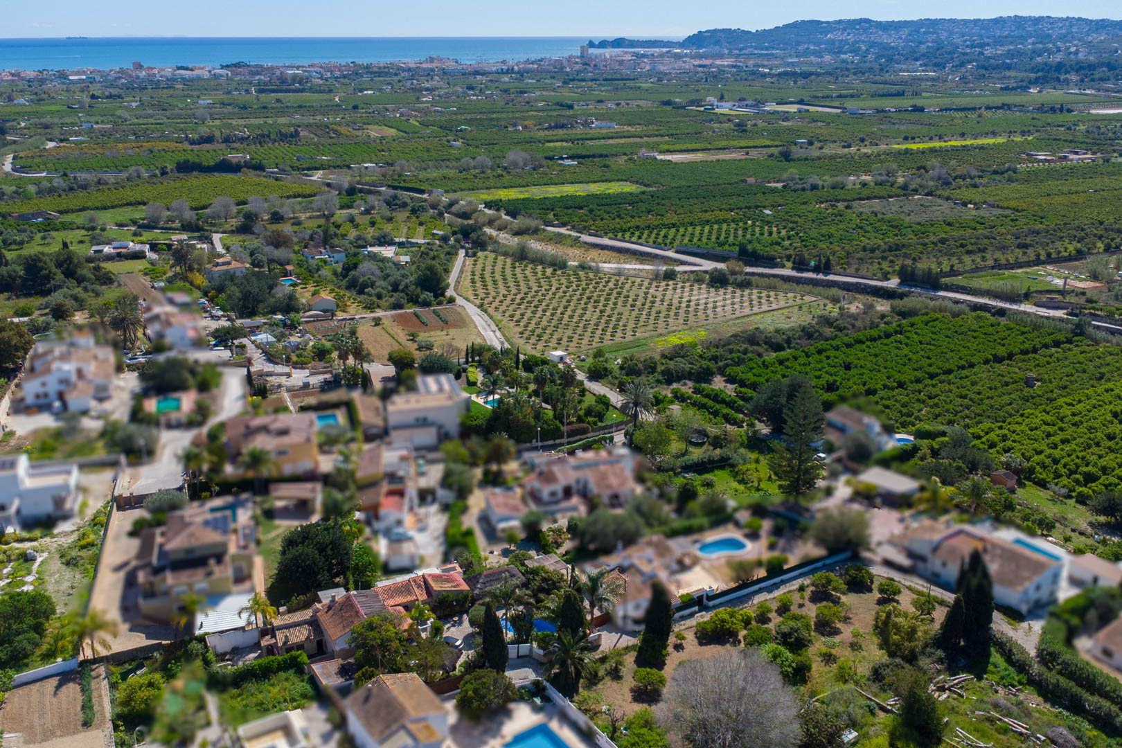 Luchtfoto van de locatie van de woning te midden van boomgaarden, met de Middellandse Zeekust en de baai van Jávea aan de horizon.