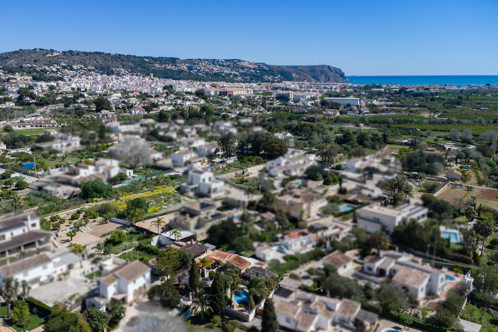 Luchtfoto van de woonwijk in Jávea, met de nabijheid van het stadscentrum, de Middellandse Zeekust en de omliggende heuvels.