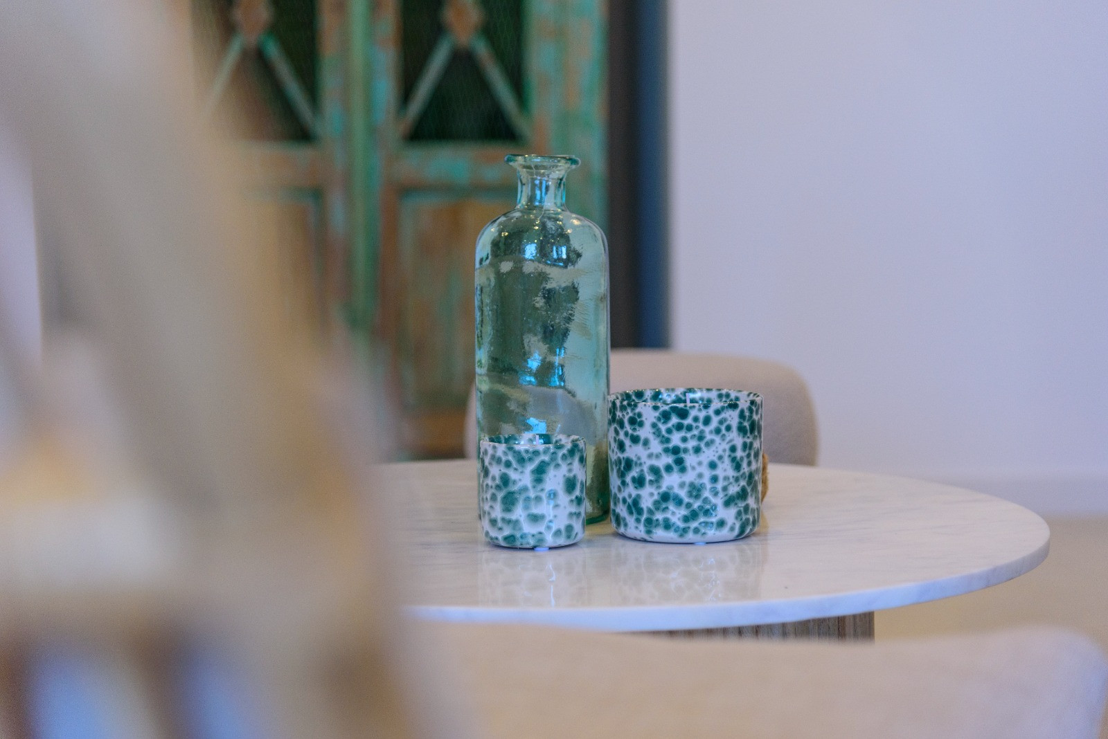 Decoratief detail op een witte marmeren tafel met een turquoise glazen fles en gedessineerde keramieken potten tegen een rustieke achtergrond.