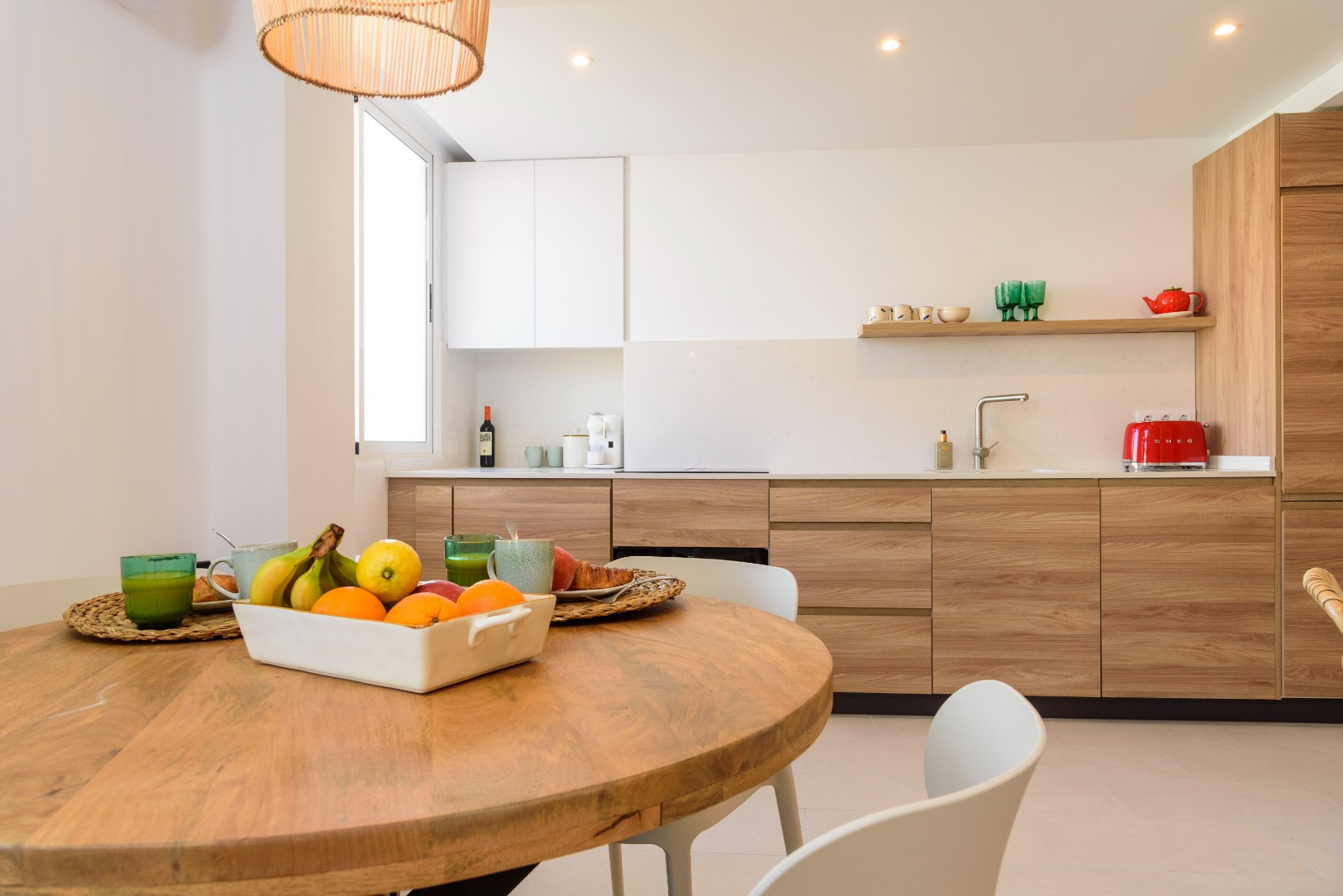 Eethoek met een ronde houten tafel en een open keuken met eikenhouten kasten, wit aanrechtblad en subtiele inbouwverlichting voor een modern geheel.