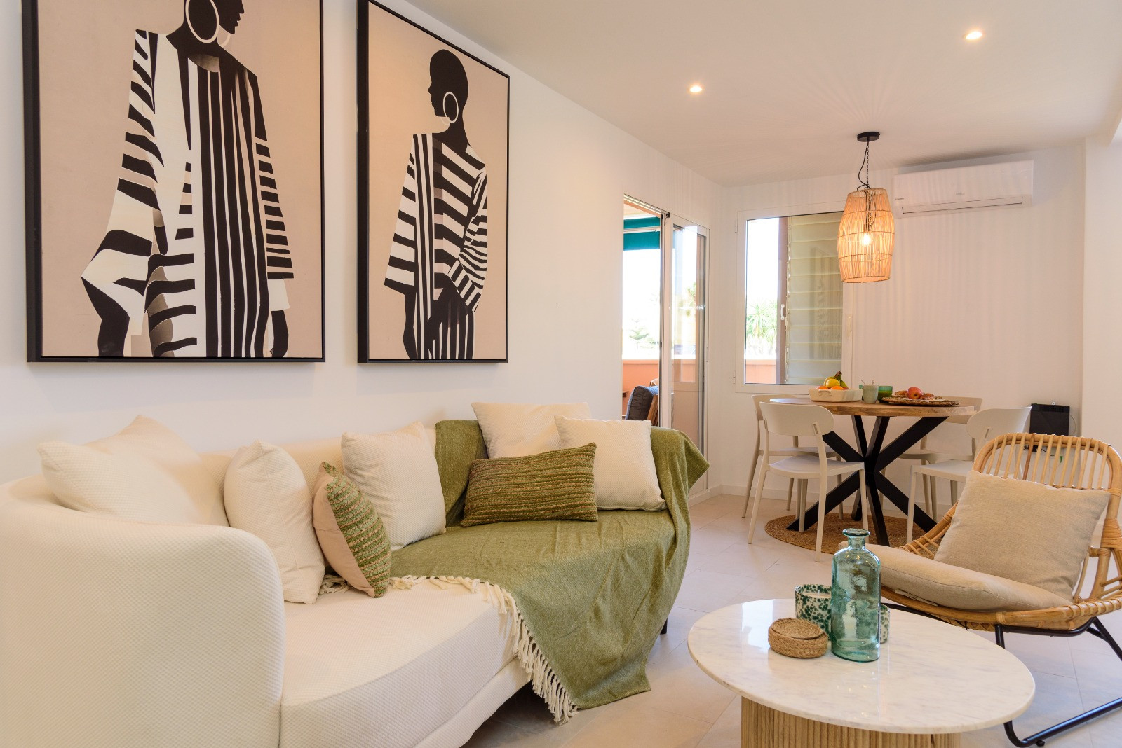 Eigentijdse woon- en eetkamer met een neutrale bank, moderne kunst en een ronde eettafel. De glazen deur biedt direct toegang tot het terras en veel lichtinval.