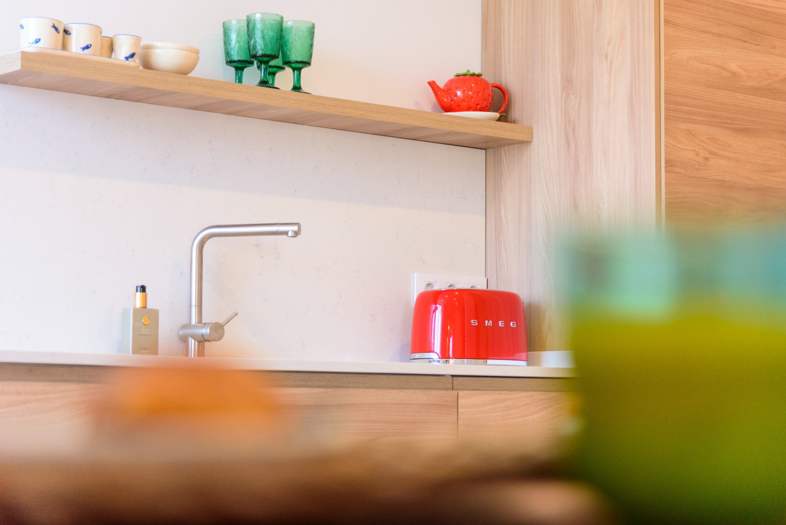 Keukendetail met wit stenen werkblad, minimalistische kraan en houten legplank. Voorzien van designapparatuur en afwerkingen in natuurlijke tinten.