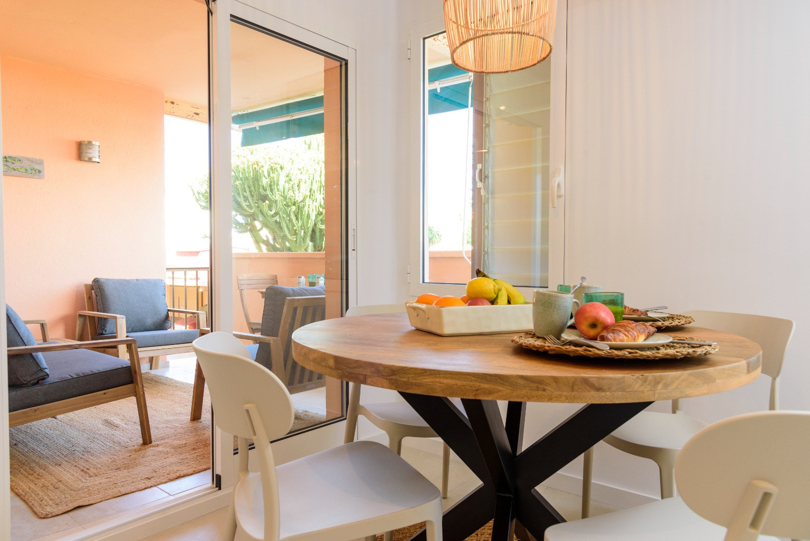 Lichte eethoek met een ronde houten tafel en witte stoelen, direct verbonden met een gemeubileerd terras via grote glazen schuifdeuren voor optimaal daglicht.