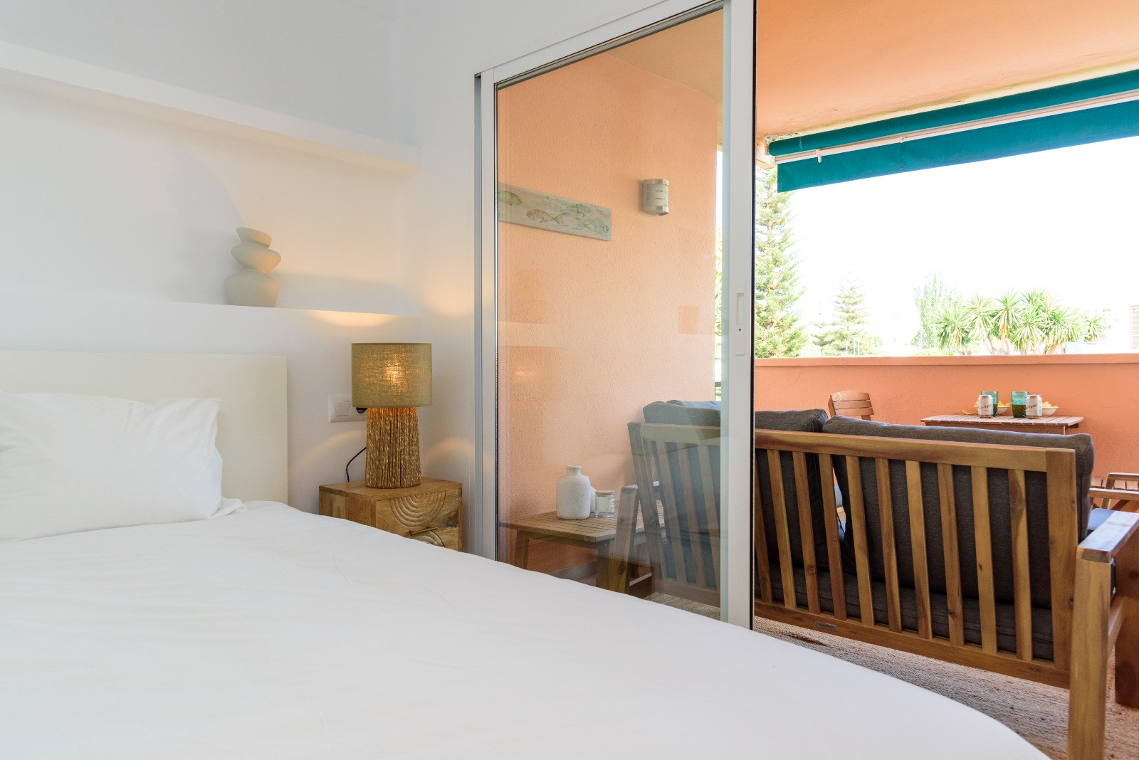 Lichte slaapkamer met directe toegang tot een privéterras met houten meubilair. De ruimte kenmerkt zich door natuurlijk licht en een minimalistisch ontwerp.