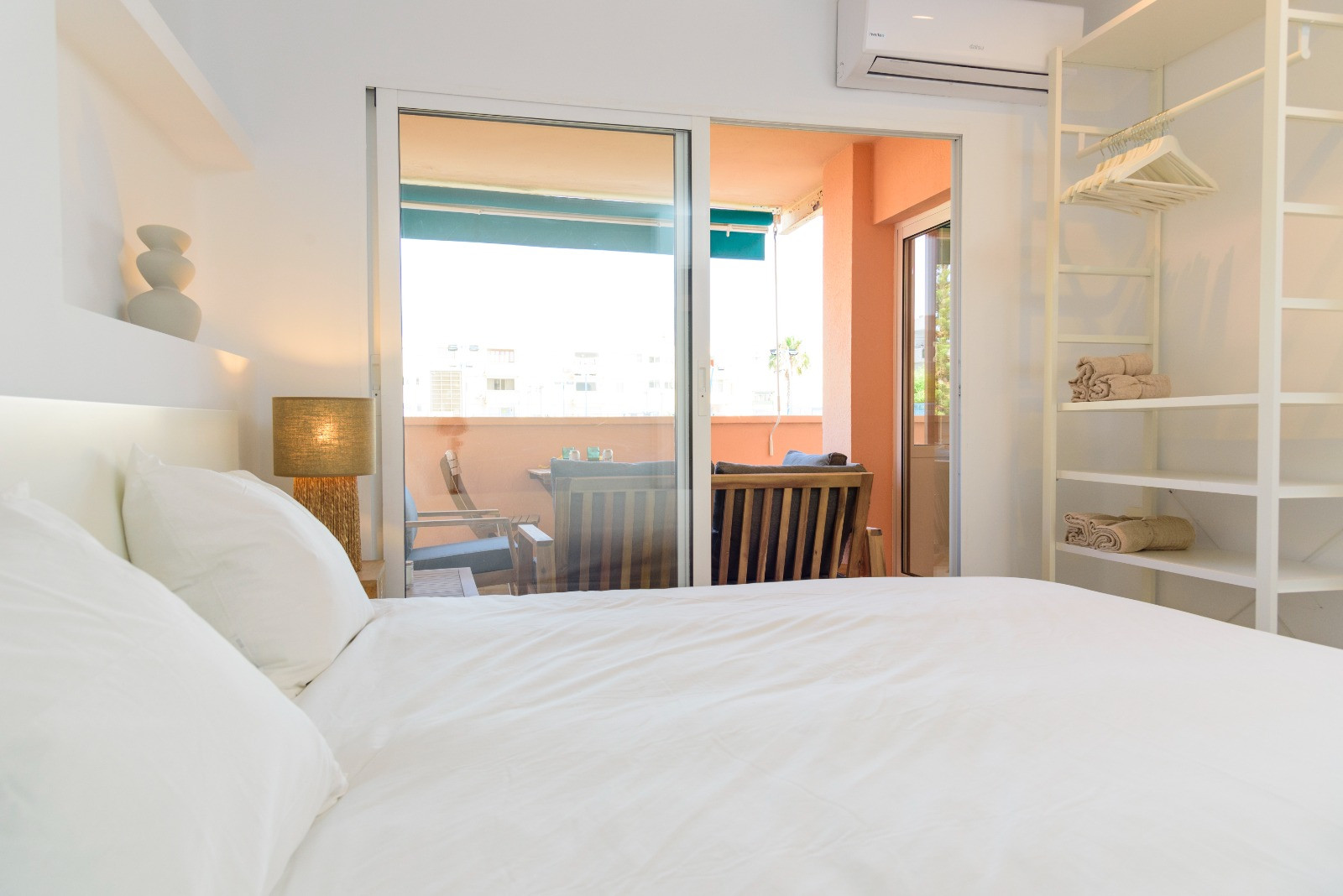Lichte slaapkamer met directe toegang tot het gemeubileerde terras, een minimalistisch open kastsysteem en split-airconditioning.