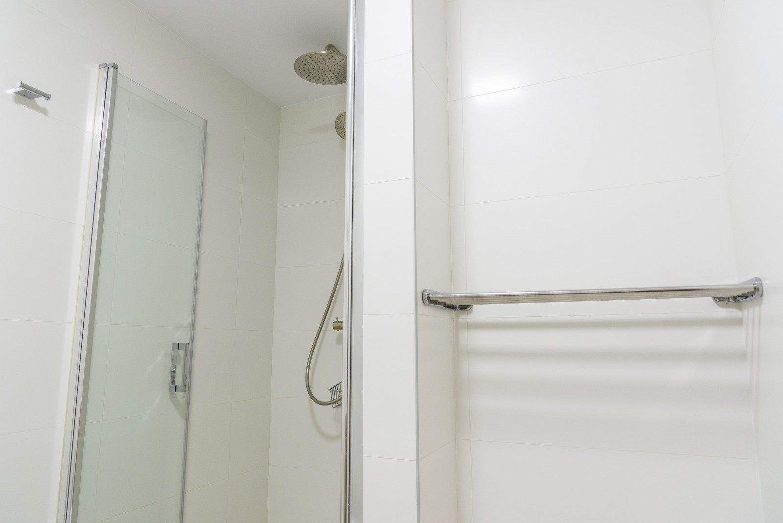 Moderne badkamer met inloopdouche, glazen wand en chromen kranen inclusief regendouche. Afgewerkt met witte wandtegels en een geïntegreerd metalen handdoekrek.