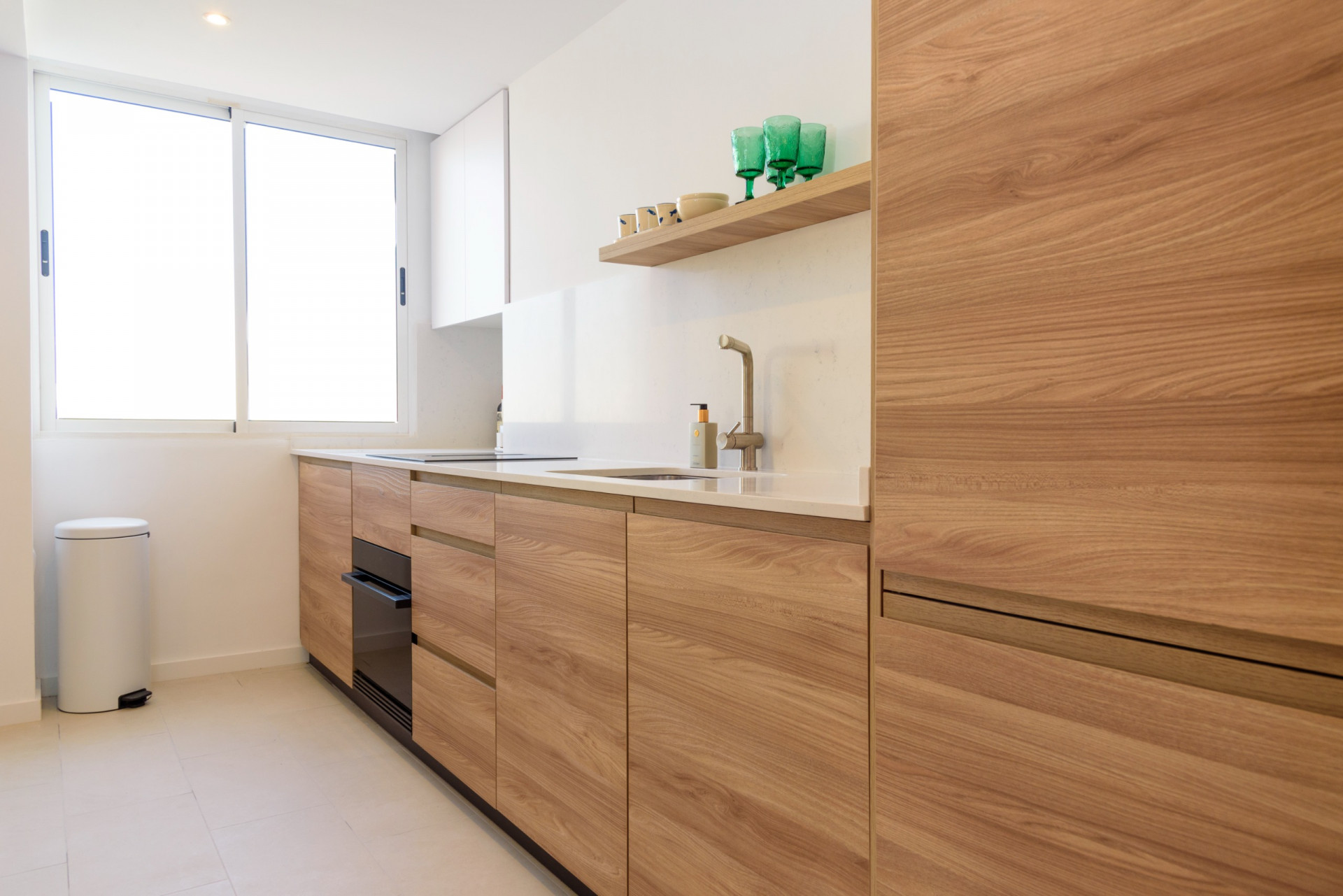 Moderne keuken met houten kasten, een wit werkblad en een geïntegreerde spoelbak. Een groot raam zorgt voor veel natuurlijk licht en benadrukt het strakke, functionele ontwerp.