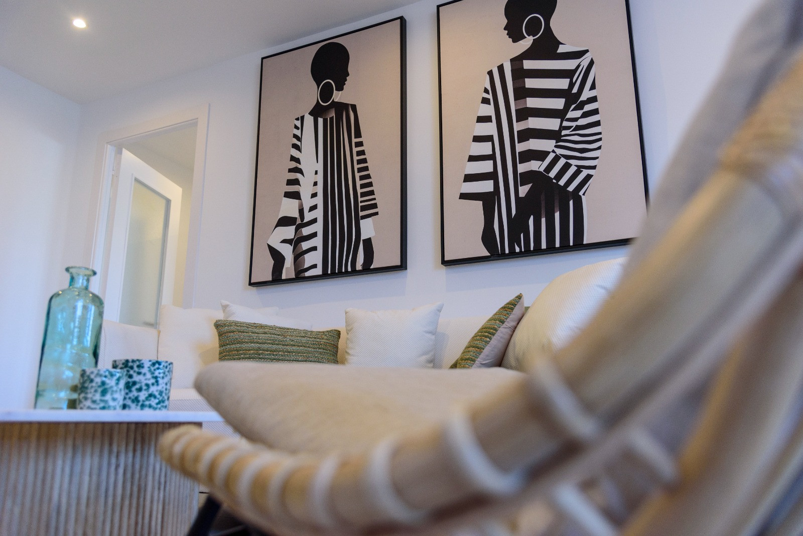 Moderne woonkamer met witte banken, getextureerde kussens en minimalistische kunst. Een houten salontafel met ribbelprofiel vormt een stijlvol middelpunt in de ruimte.