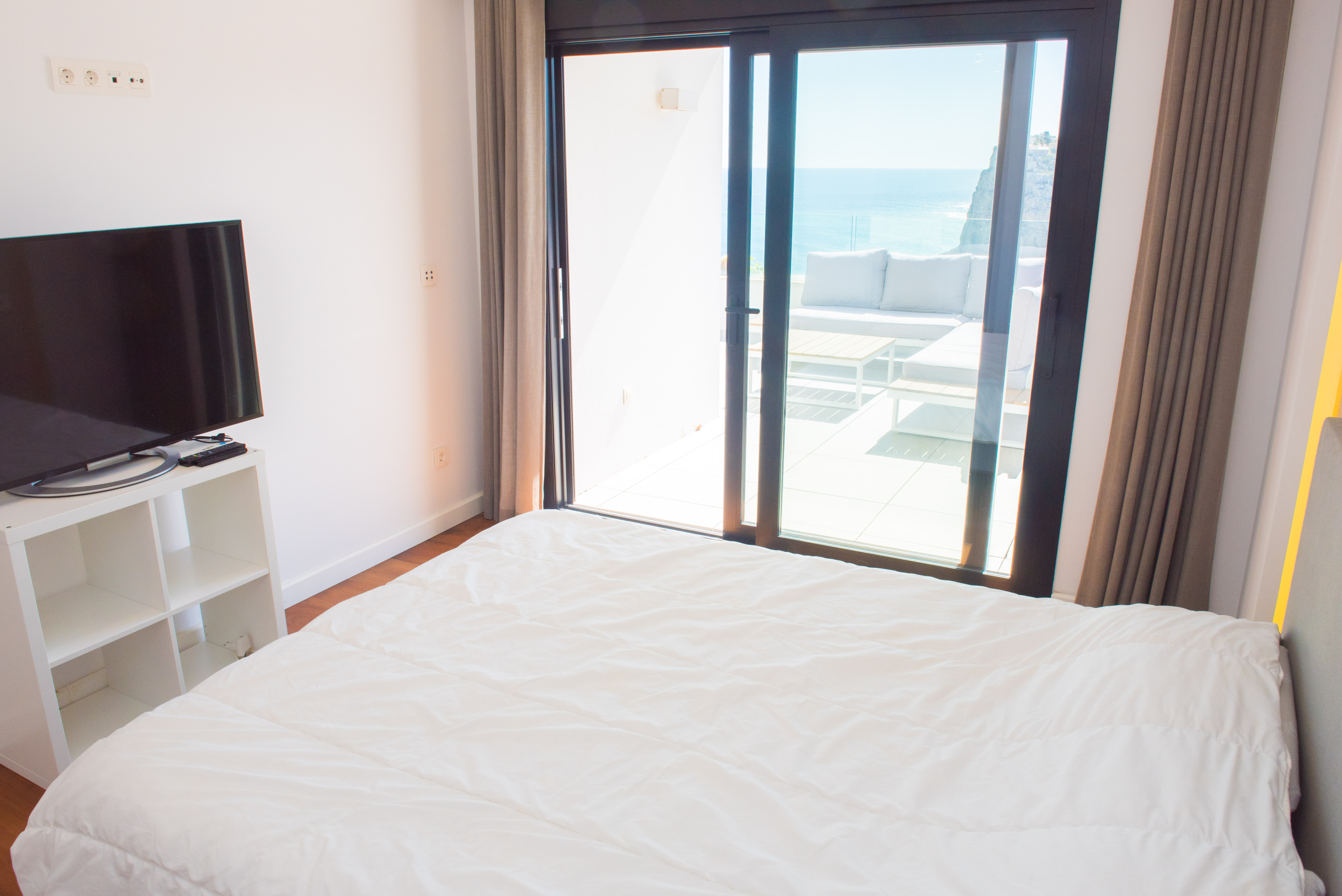 Lichte slaapkamer met directe toegang tot een privéterras met loungeset en panoramisch uitzicht over de Middellandse Zee en de omliggende kliffen.