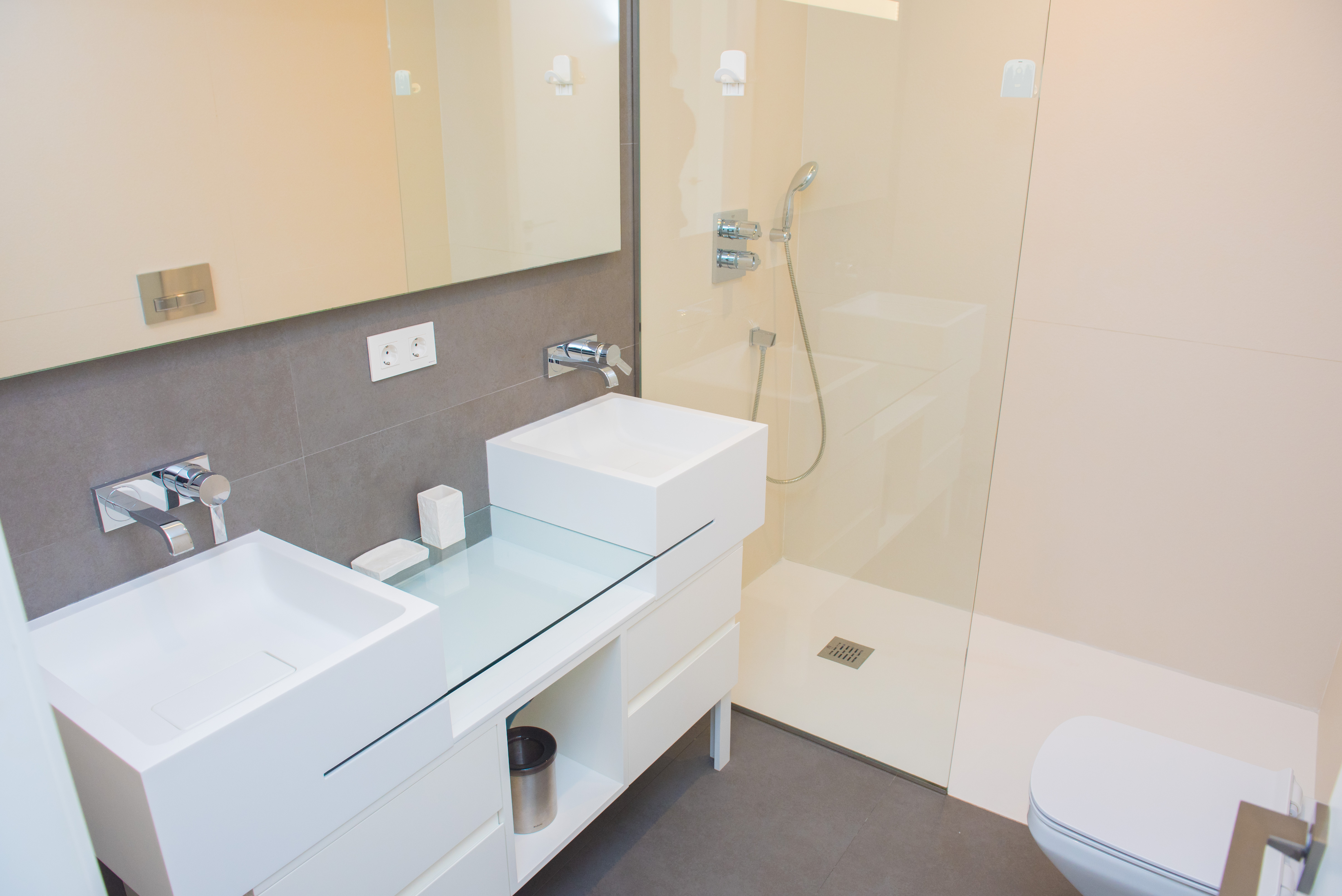 Moderne badkamer met dubbele wastafel, vierkante opzetkommen, chromen inbouwkranen en een inloopdouche met glazen wand.