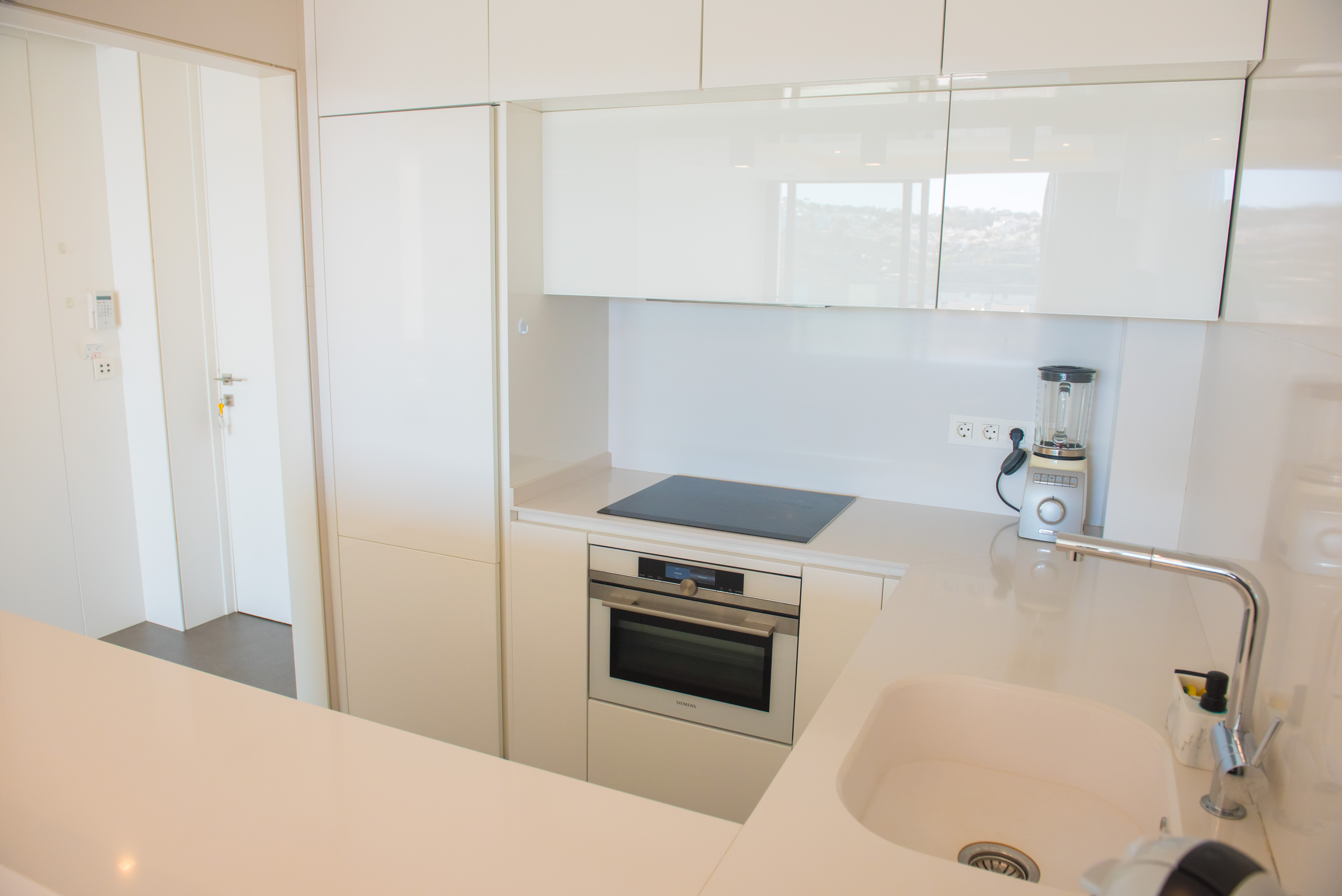 Moderne keuken met witglanzende kasten, geïntegreerde Siemens oven, inductiekookplaat en wit kwarts werkblad met onderbouw spoelbak.