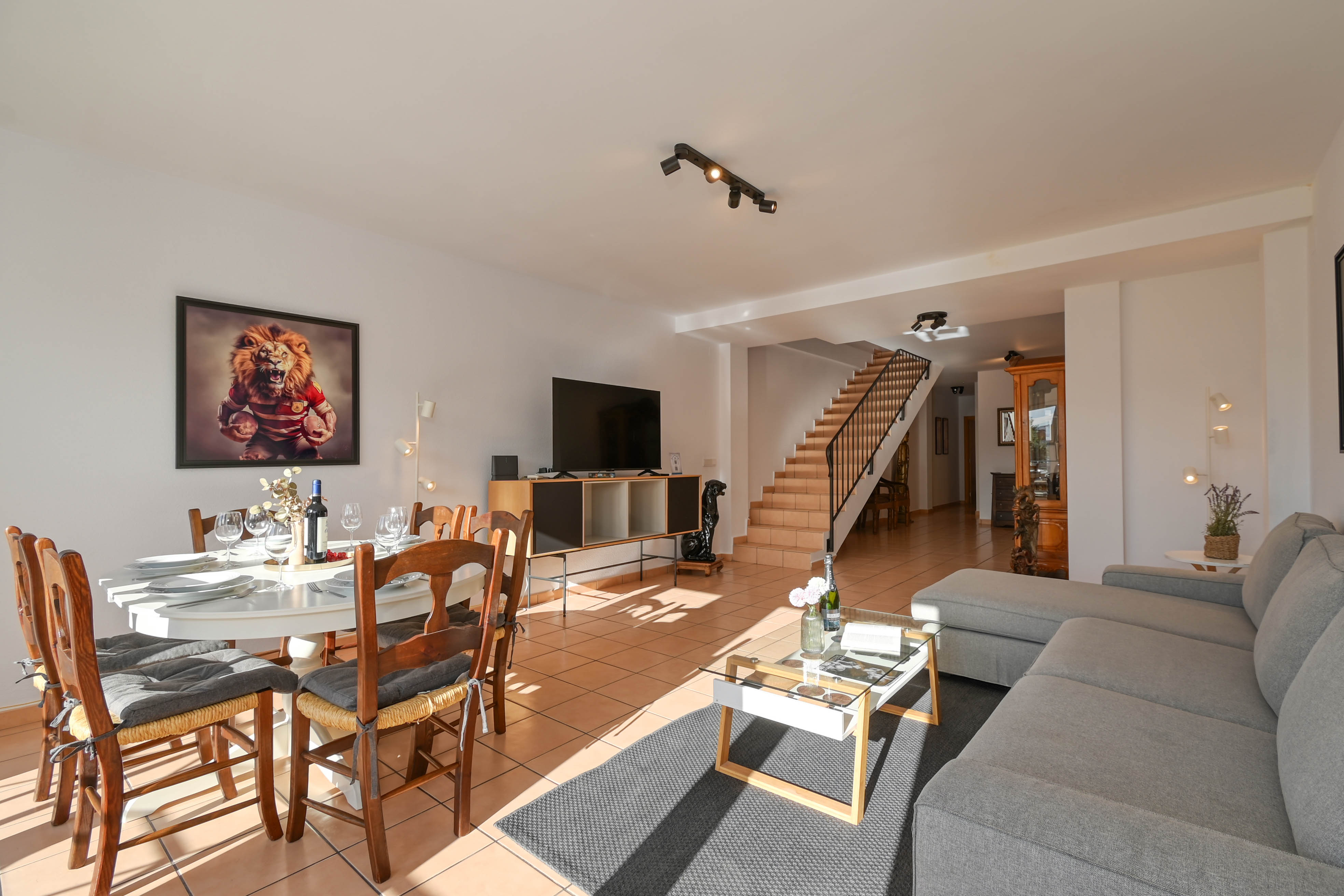 Open woonruimte met terracotta vloer, een grijze hoekbank en een trap met metalen leuning die naar de bovenverdieping van het appartement leidt.