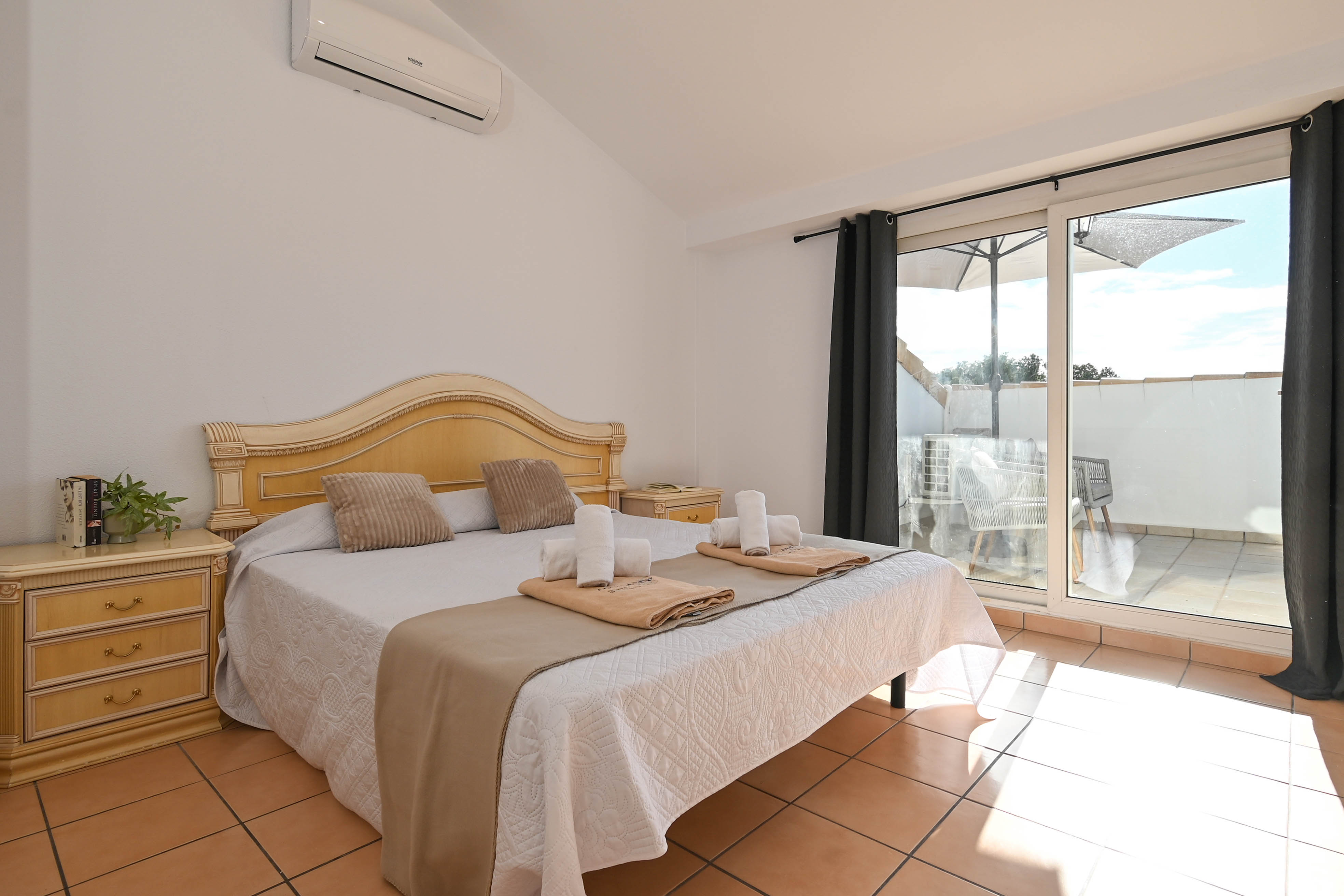 Slaapkamer met schuine plafonds, airconditioning en directe toegang tot het terras. Voorzien van een terracotta vloer en klassiek houten meubilair.