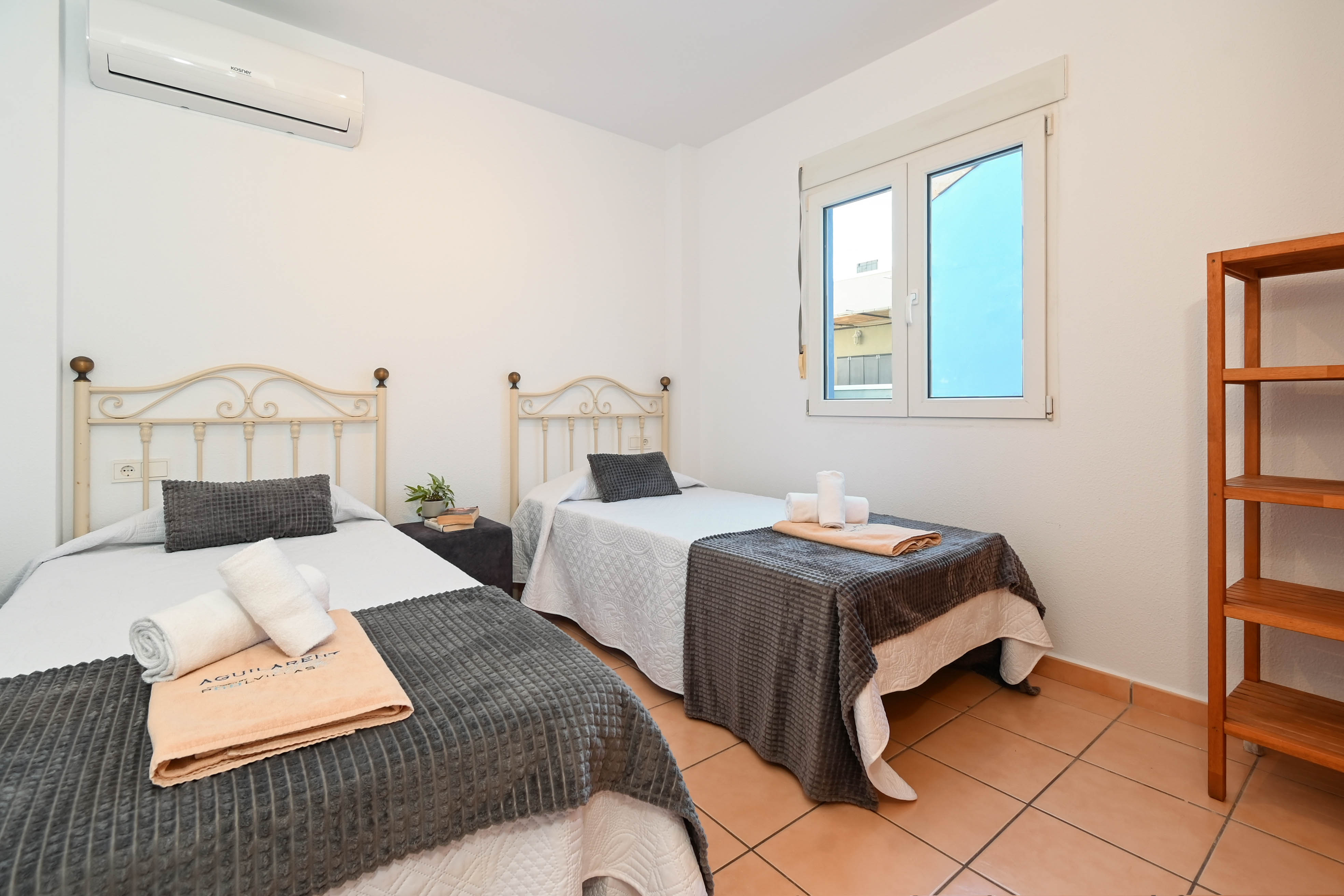 Slaapkamer met twee eenpersoonsbedden, smeedijzeren hoofdeinden, terracotta tegelvloer en airconditioning. Voorzien van een houten stellingkast en natuurlijk licht.