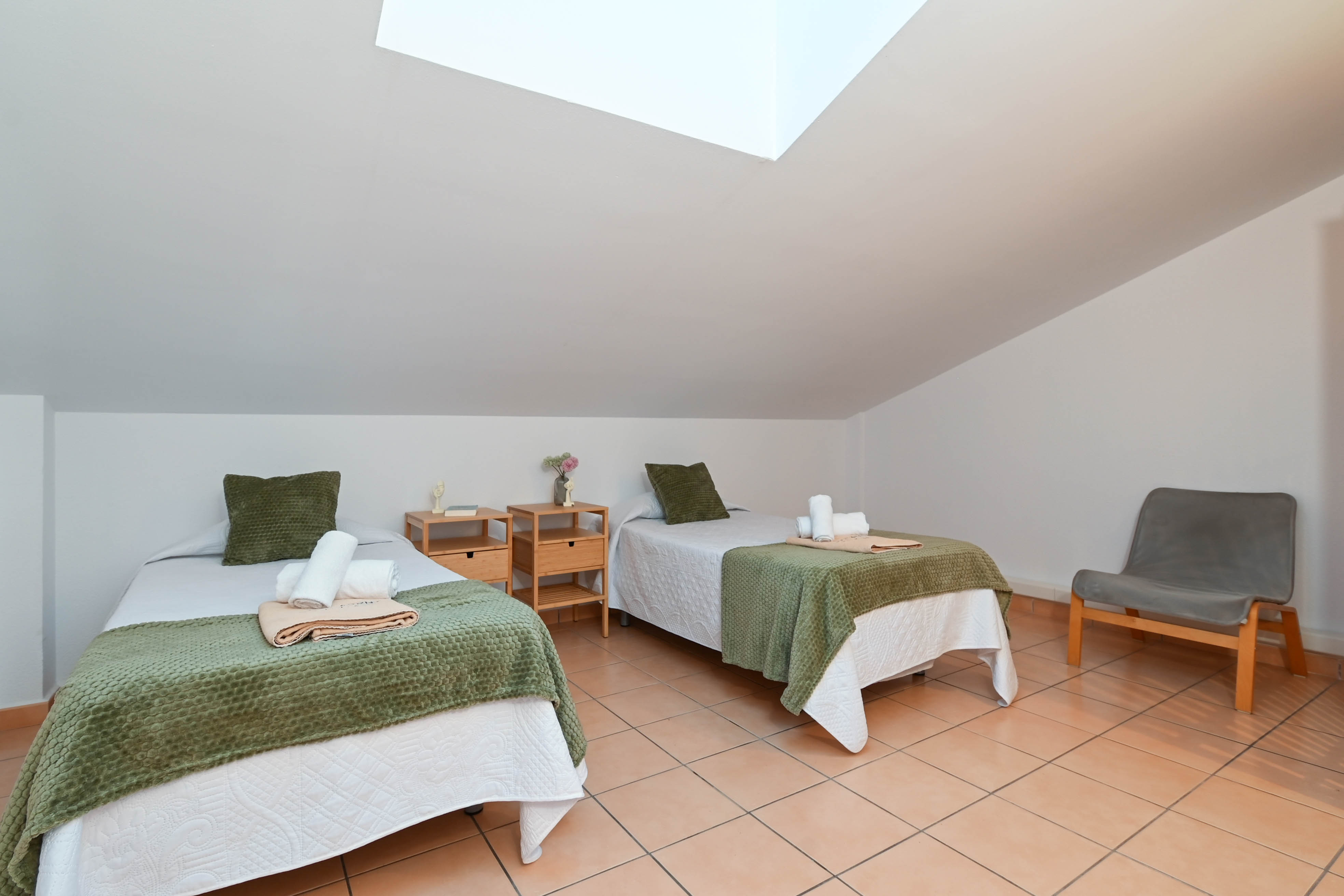 Slaapkamer onder het schuine dak met twee eenpersoonsbedden, terracotta vloertegels en een dakraam voor optimale natuurlijke lichtinval.