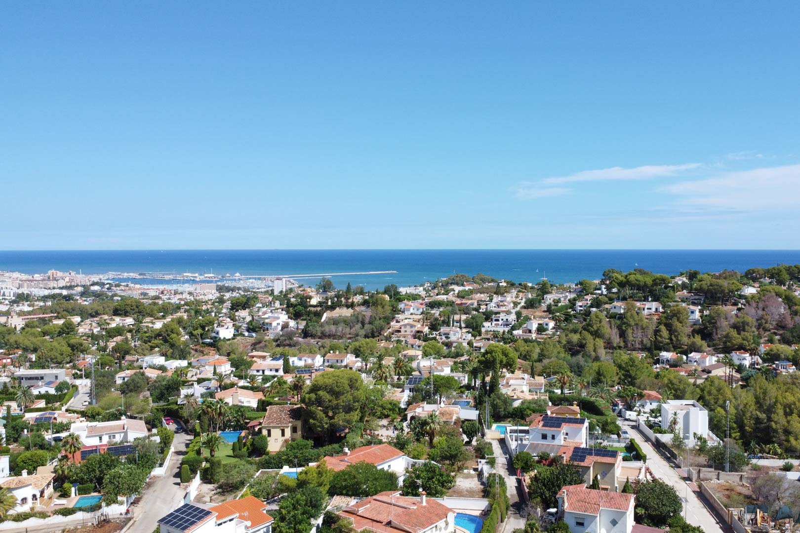 Panoramisch luchtfoto van de woonwijk in Dénia met uitzicht op de Middellandse Zee, de haven en een gevestigde omgeving van vrijstaande woningen met zwembaden.
