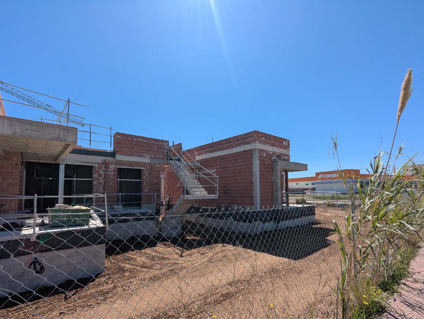 Buitenaanzicht van de villa in aanbouw, met de bakstenen structuur, betonnen trap en de gunstige ligging nabij commerciële voorzieningen.