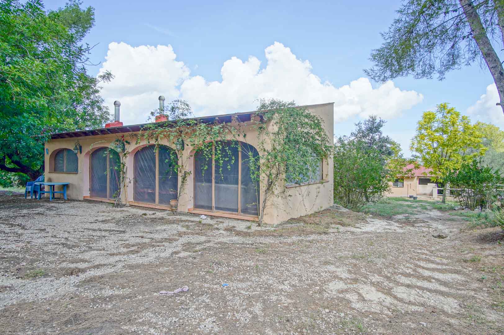 Bijgebouw met boogvormige openingen en houten balken, gelegen op een natuurlijk perceel met pijnbomen en mediterrane beplanting in Orba.