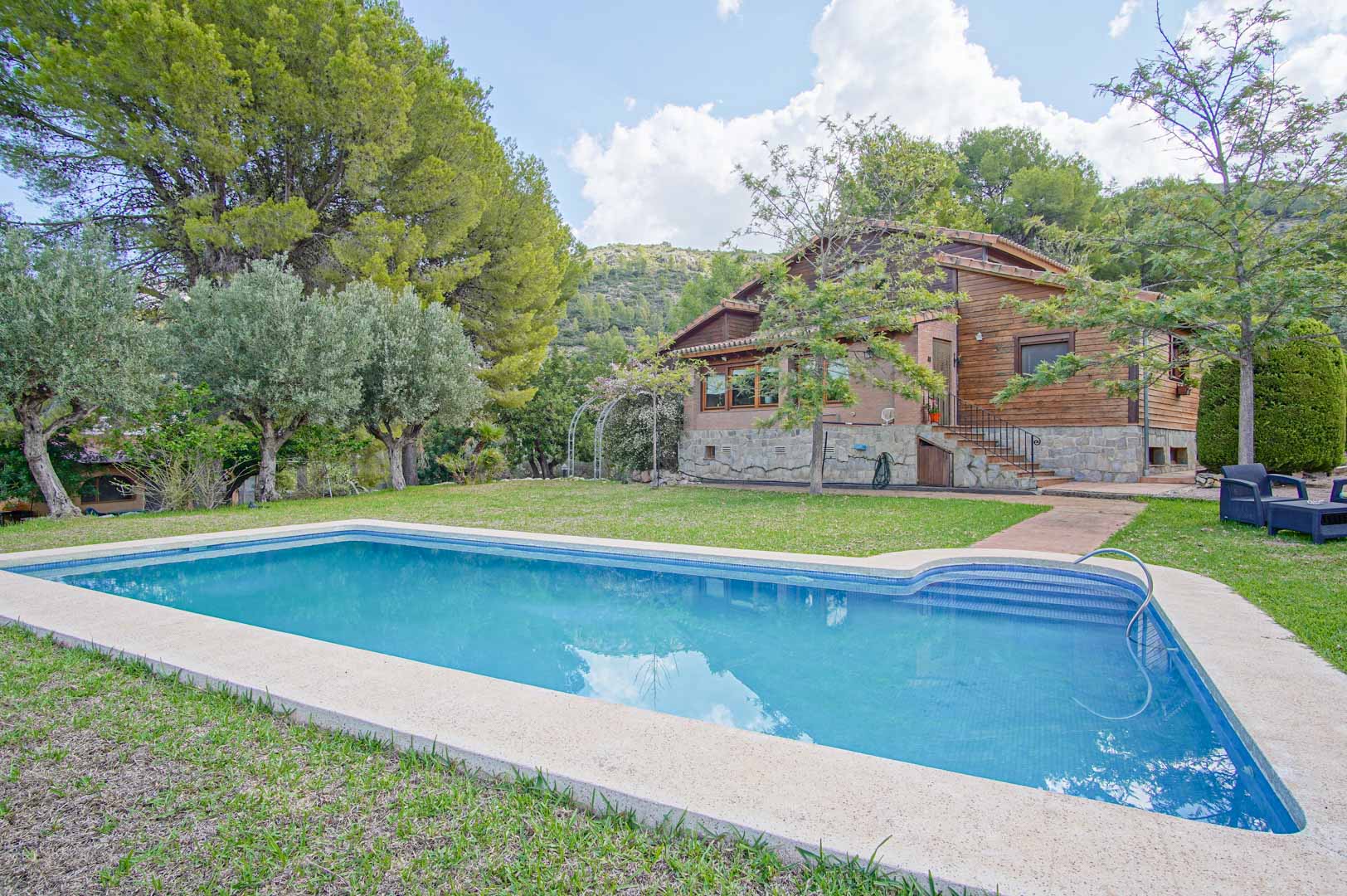 Buitenaanzicht van de villa met een rechthoekig zwembad en gazon. De gevel van Fins vurenhout en natuursteen wordt omringd door mediterrane dennen en bergen.