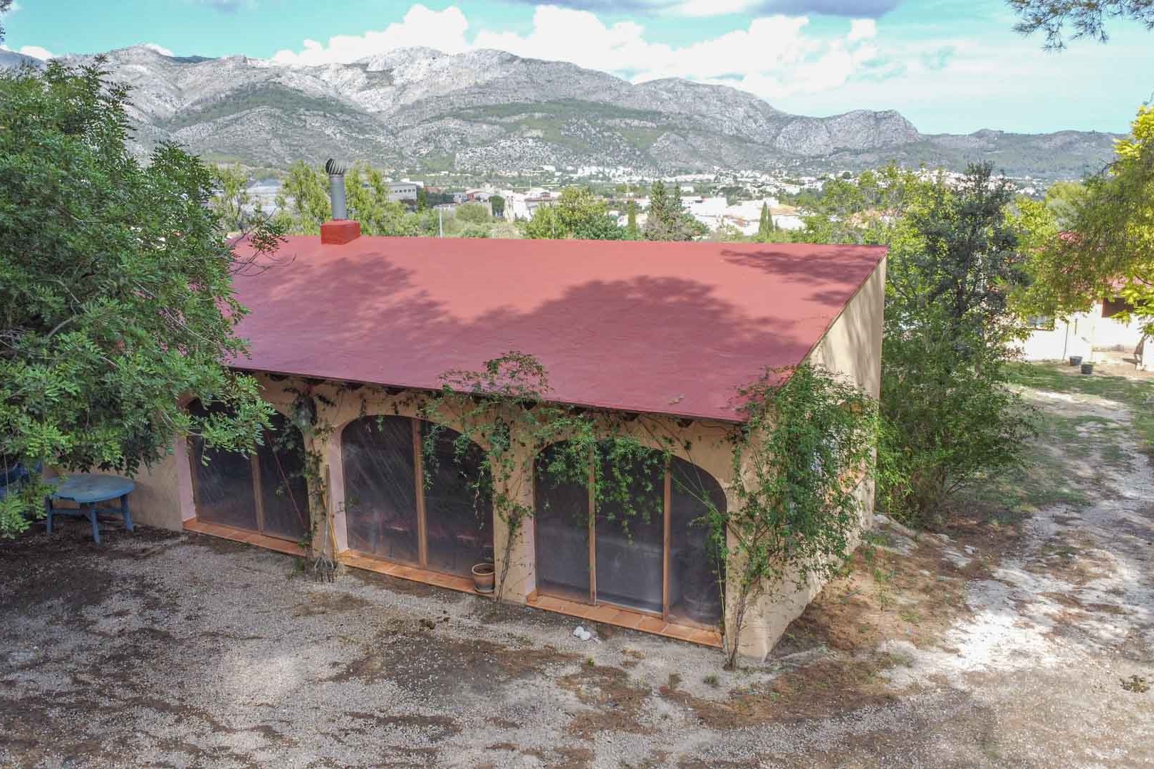 Exterieur van het bijgebouw met karakteristieke boogvensters en een schoorsteen, omgeven door groen met een panoramisch uitzicht op de bergen en de vallei.