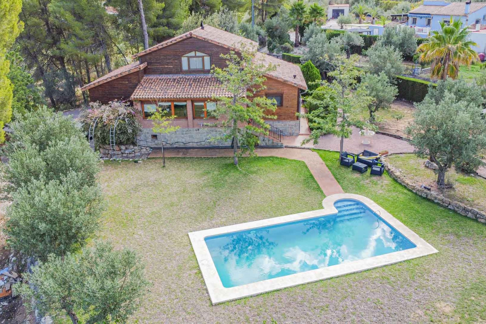 Luchtfoto van de villa met houten en stenen gevel, voorzien van een privézwembad omgeven door een gazon en mediterrane olijfbomen.