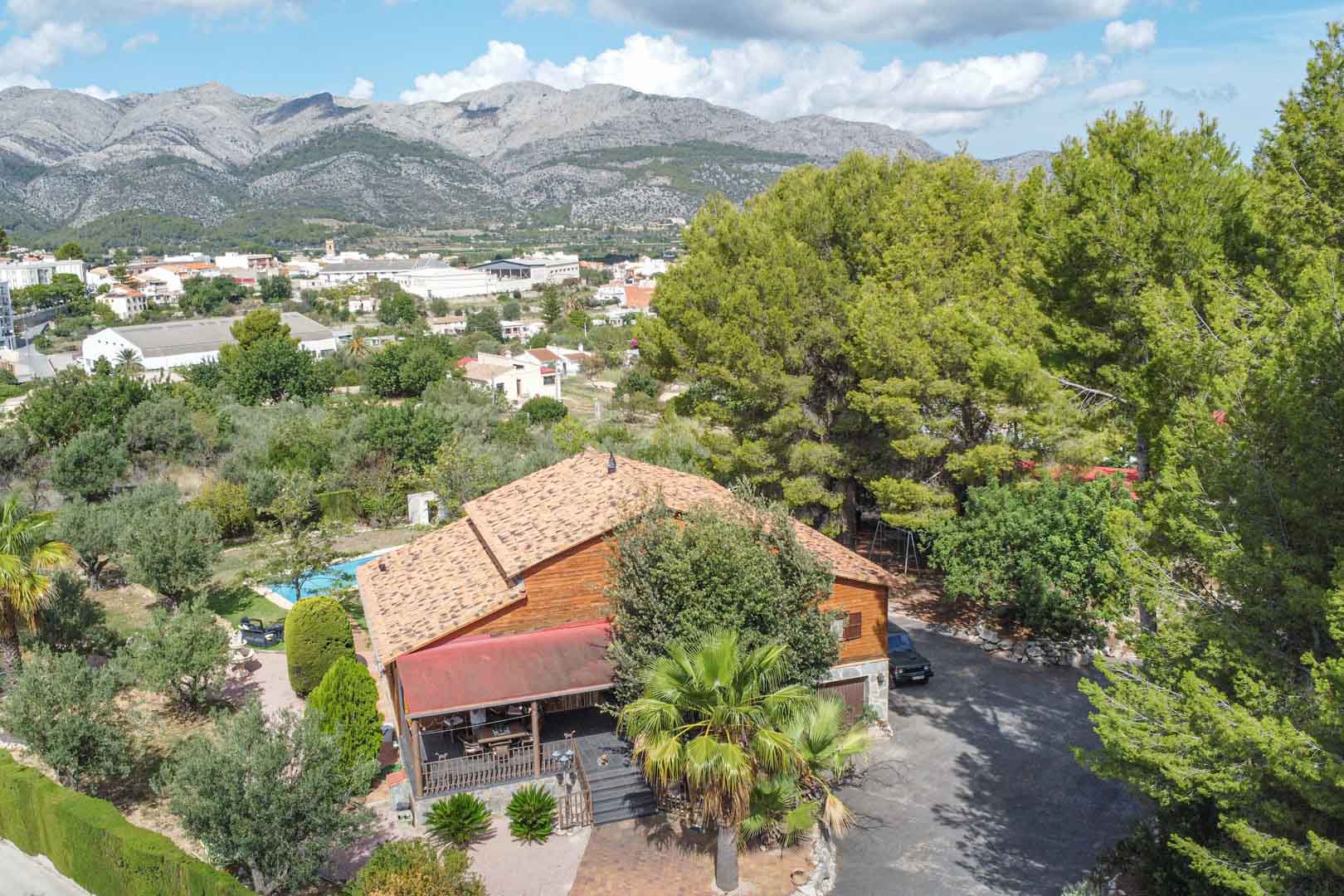 Luchtfoto van de villa van Fins vurenhout, omgeven door mediterrane beplanting met uitzicht op de bergen en het nabijgelegen dorp Orba.