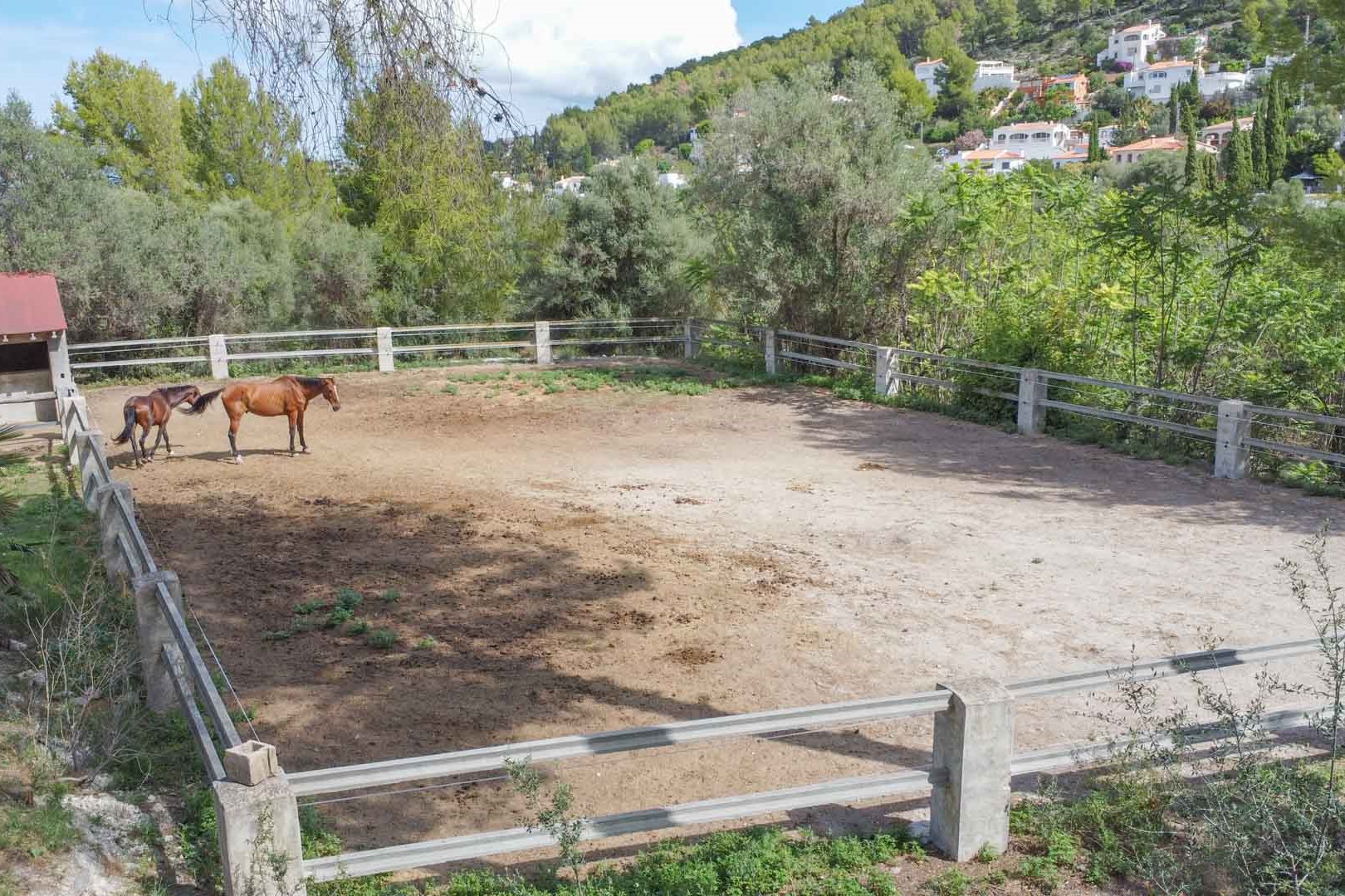 Omheinde paardenbak met stenen palen, gelegen op een uitgestrekt perceel omringd door mediterrane beplanting en uitzicht op de heuvels.
