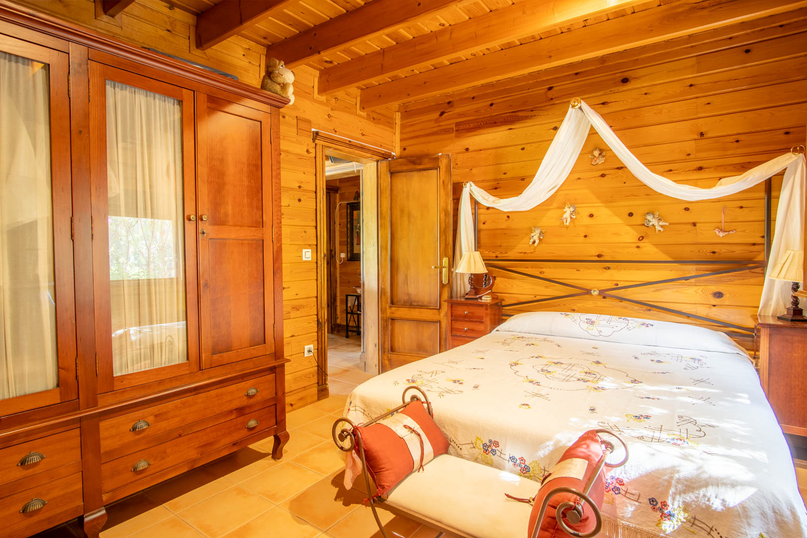 Rustieke slaapkamer met wanden en plafonds van Fins grenenhout, een massief houten kledingkast en een tweepersoonsbed met decoratieve hemel en smeedijzeren hoofdbord.