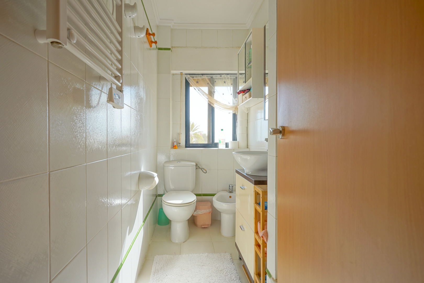 Functionele badkamer met witte tegels, een bidet, toilet en een wastafelmeubel. Een raam zorgt voor natuurlijk licht en uitzicht op de groene omgeving.