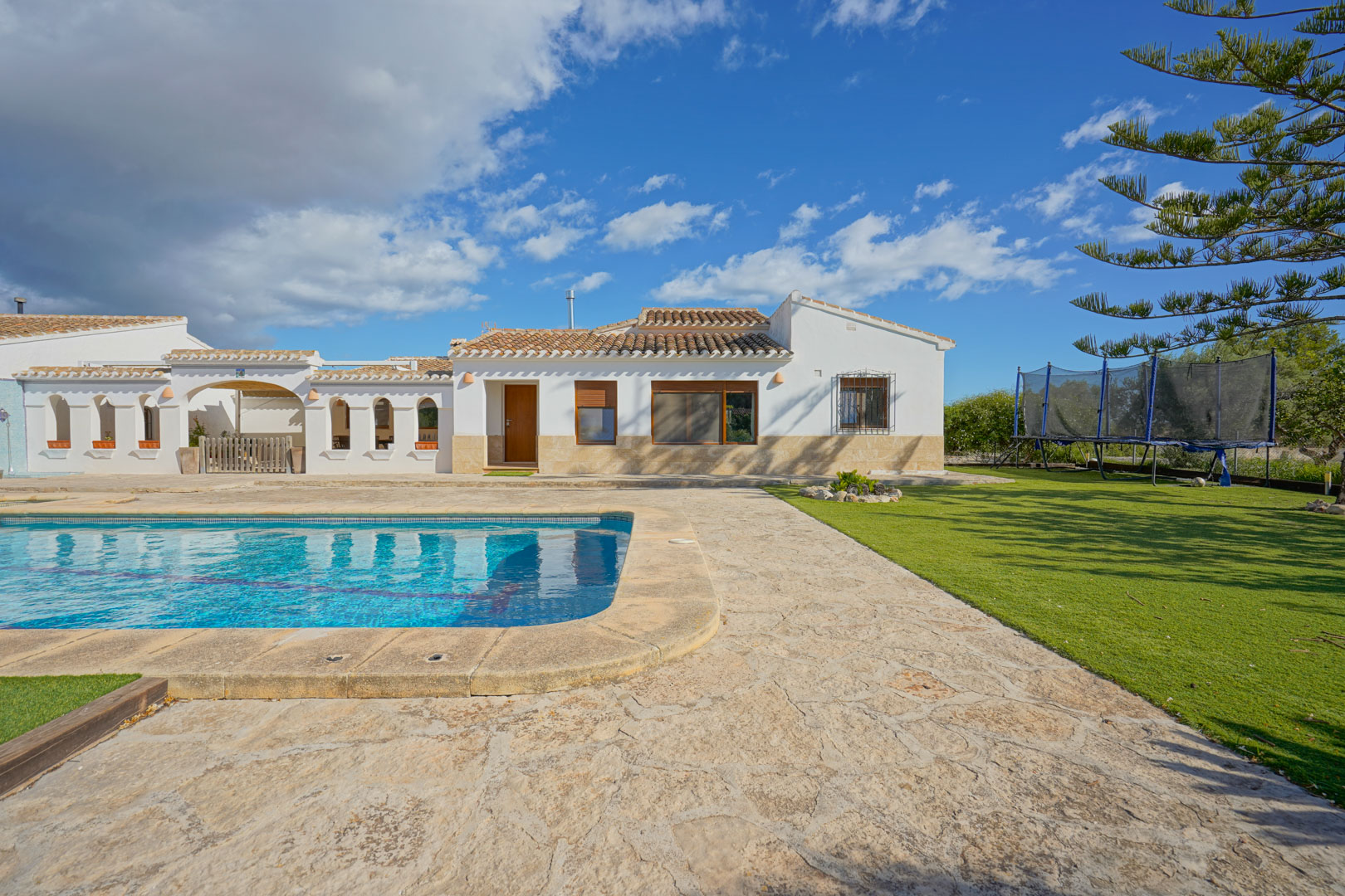 Buitenaanzicht van de villa met zwembad, natuurstenen terras en verzorgd gazon, passend bij de mediterrane architectuur met witte muren en pannendak.