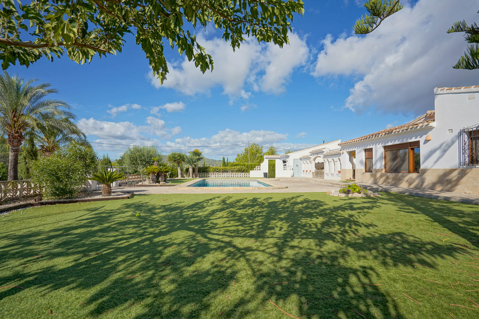 Buitenaanzicht van de witte villa met stenen plint, voorzien van een rechthoekig zwembad, zonnig terras en een verzorgd gazon met mediterrane beplanting.