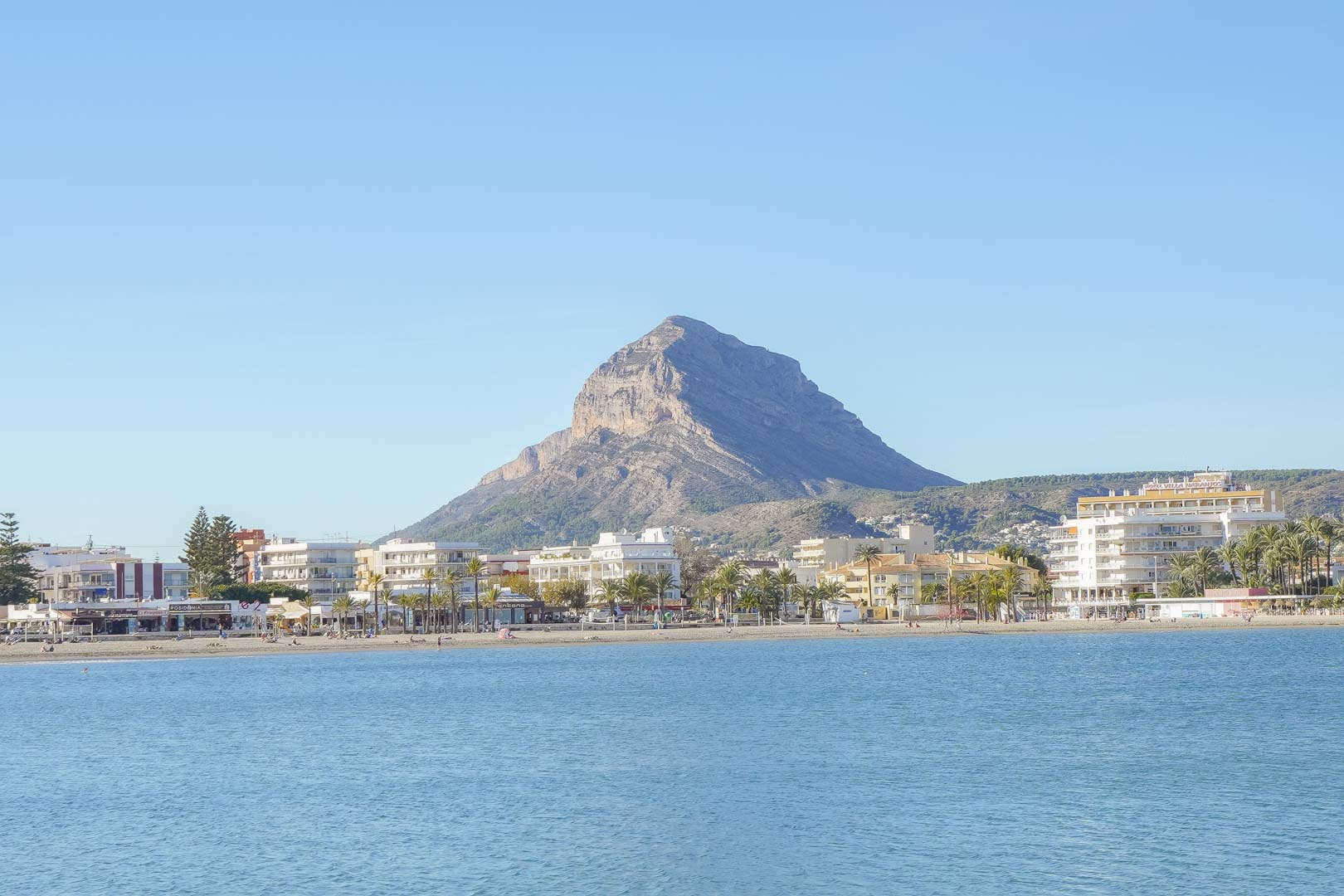 Panoramisch uitzicht op het Arenal-strand in Jávea, met de iconische Montgó-berg op de achtergrond en kustgebouwen langs de Middellandse Zee.