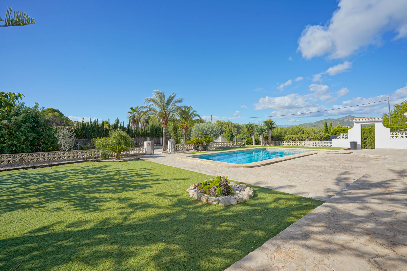 Ruime buitenruimte met rechthoekig zwembad, zonneterras in natuursteen en een verzorgd gazon met palmbomen en mediterrane beplanting.