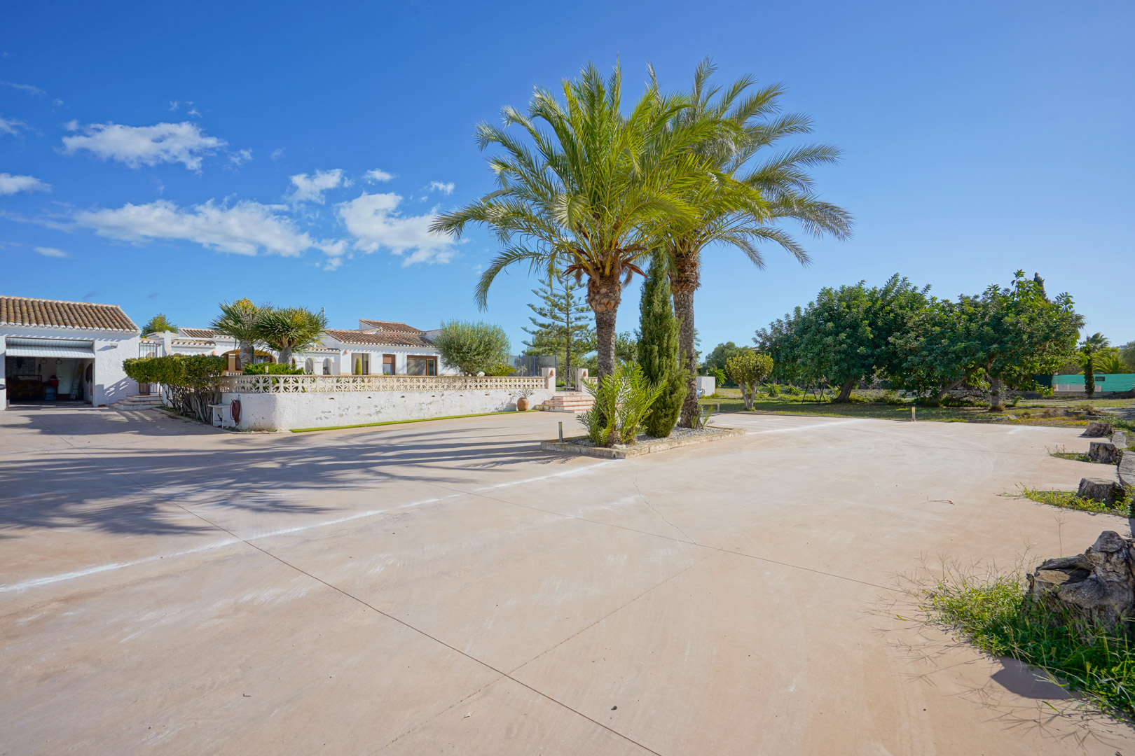 Ruime geplaveide oprit met centrale palmbomen, die directe toegang biedt tot de garage en de witte villa in mediterrane stijl.