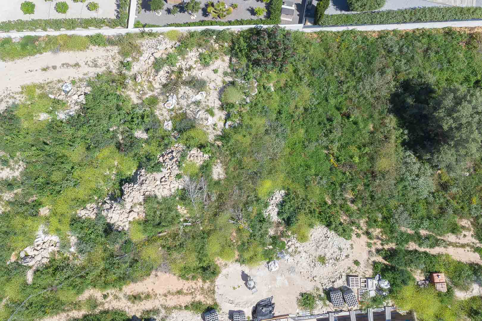 Bovenaanzicht van het perceel van meer dan 1.000 m², met natuurlijk mediterraan terrein en de eerste bouwmaterialen op de locatie.