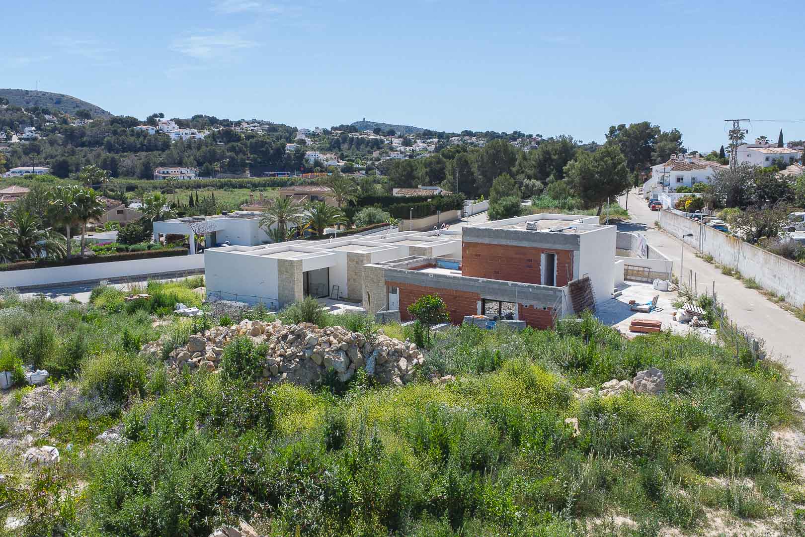 Buitenaanzicht van de villa in aanbouw, met moderne architectonische lijnen, natuurstenen gevels en baksteenstructuren in een mediterraan landschap.