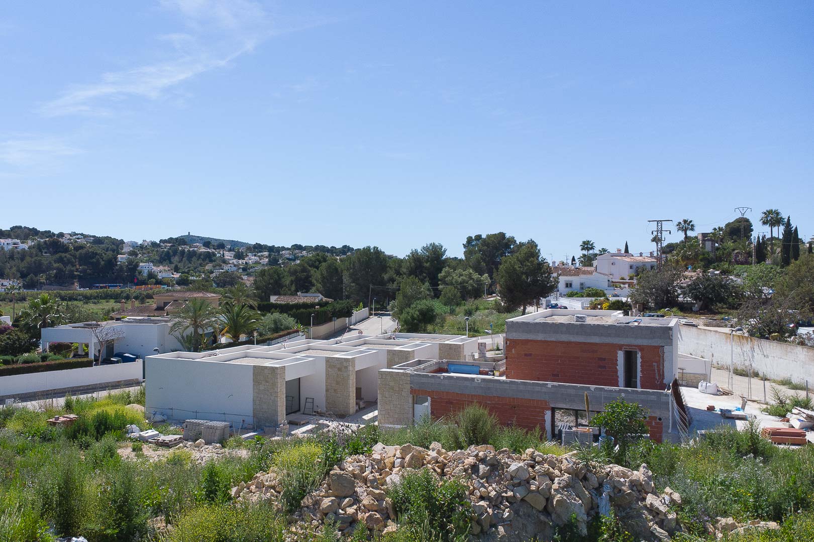 Buitenaanzicht van de woning in aanbouw, met natuurstenen details en een modern ontwerp, gelegen in het glooiende landschap van Moraira.