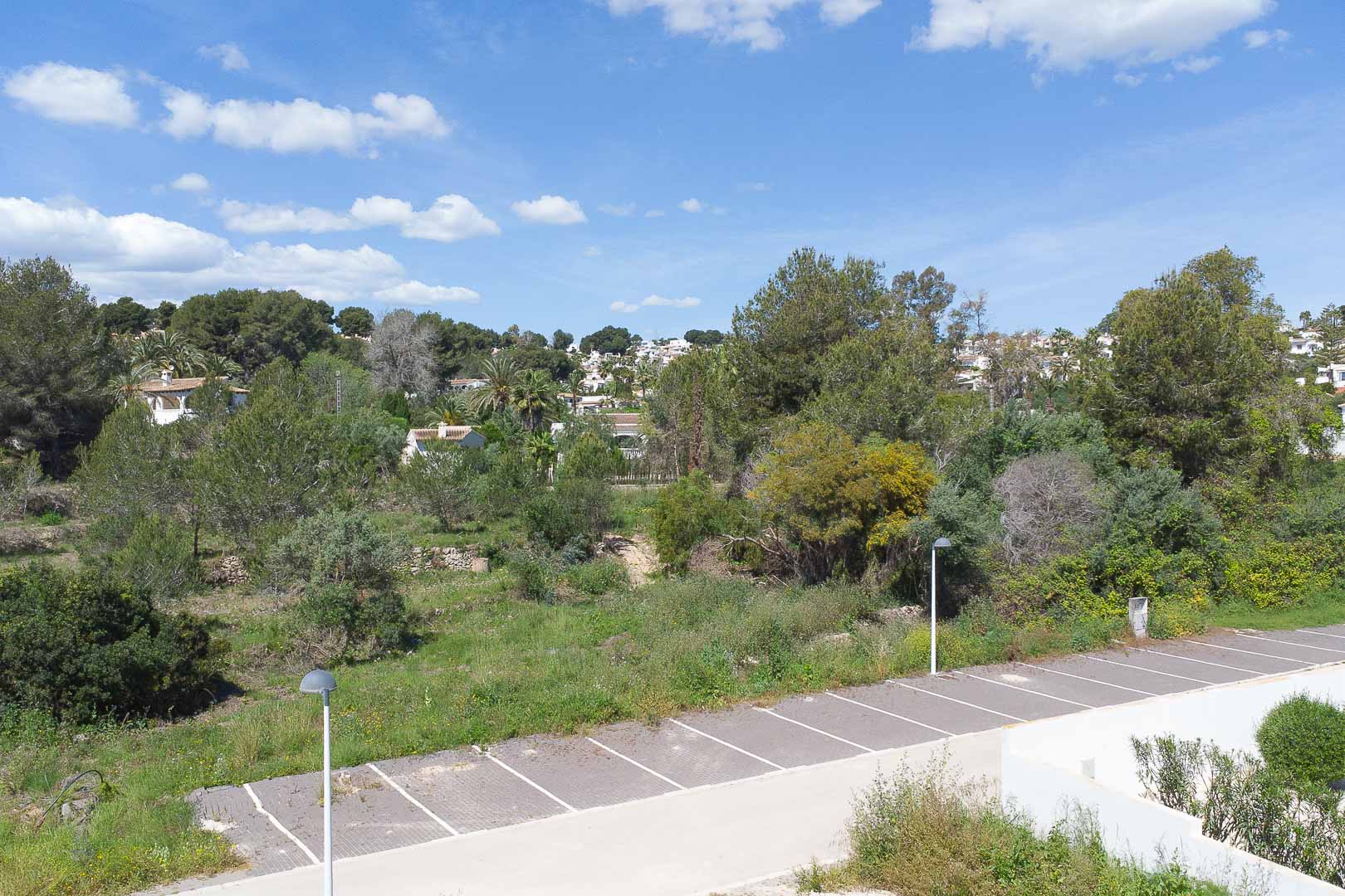 Panoramisch uitzicht vanaf het pand op het mediterrane landschap, met dichte begroeiing, omliggende woningen en een buitenparkeerplaats.