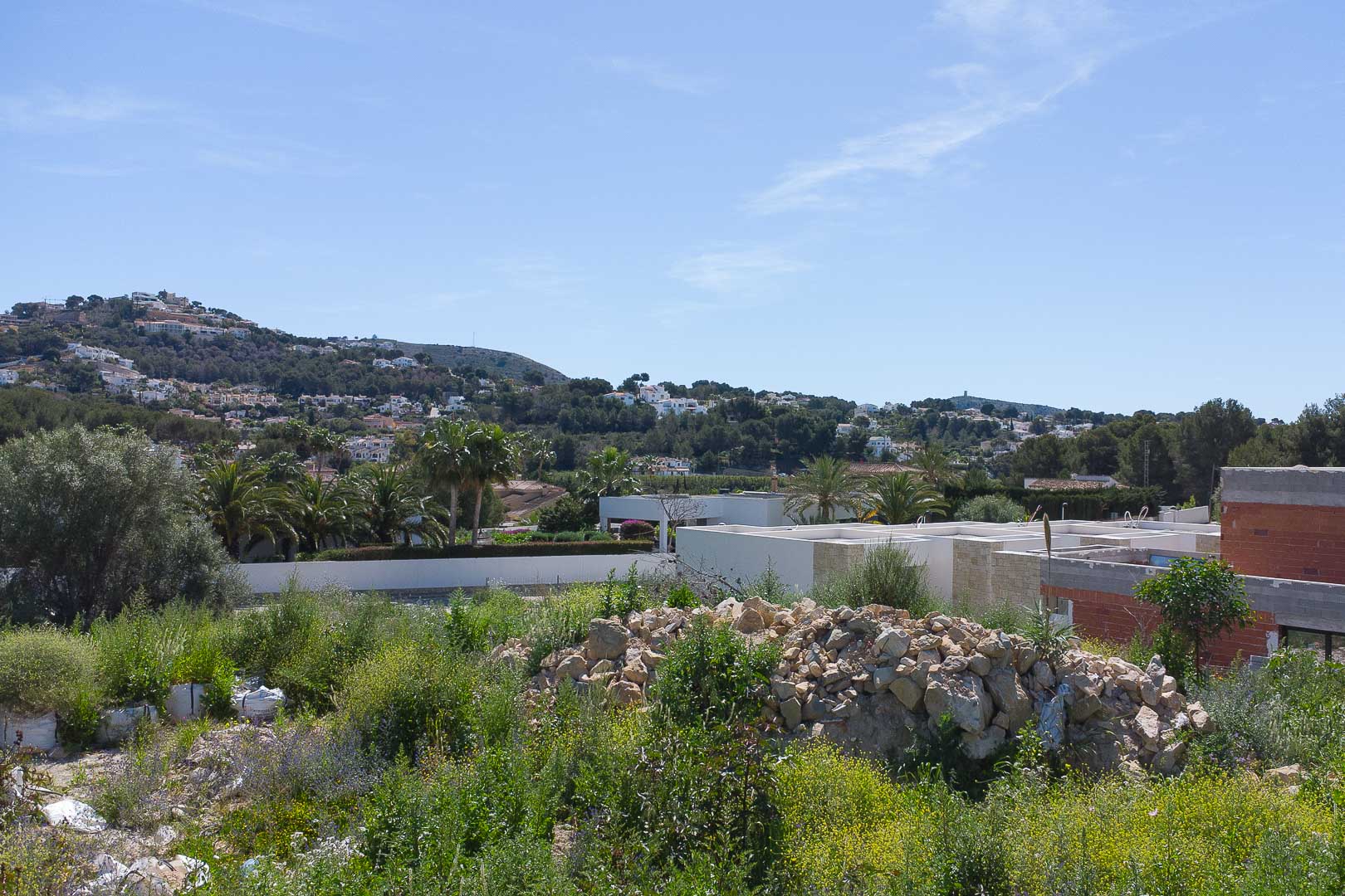 Panoramisch uitzicht vanaf het perceel op de heuvels van Moraira, met het natuurlijke landschap en de omliggende villa's.