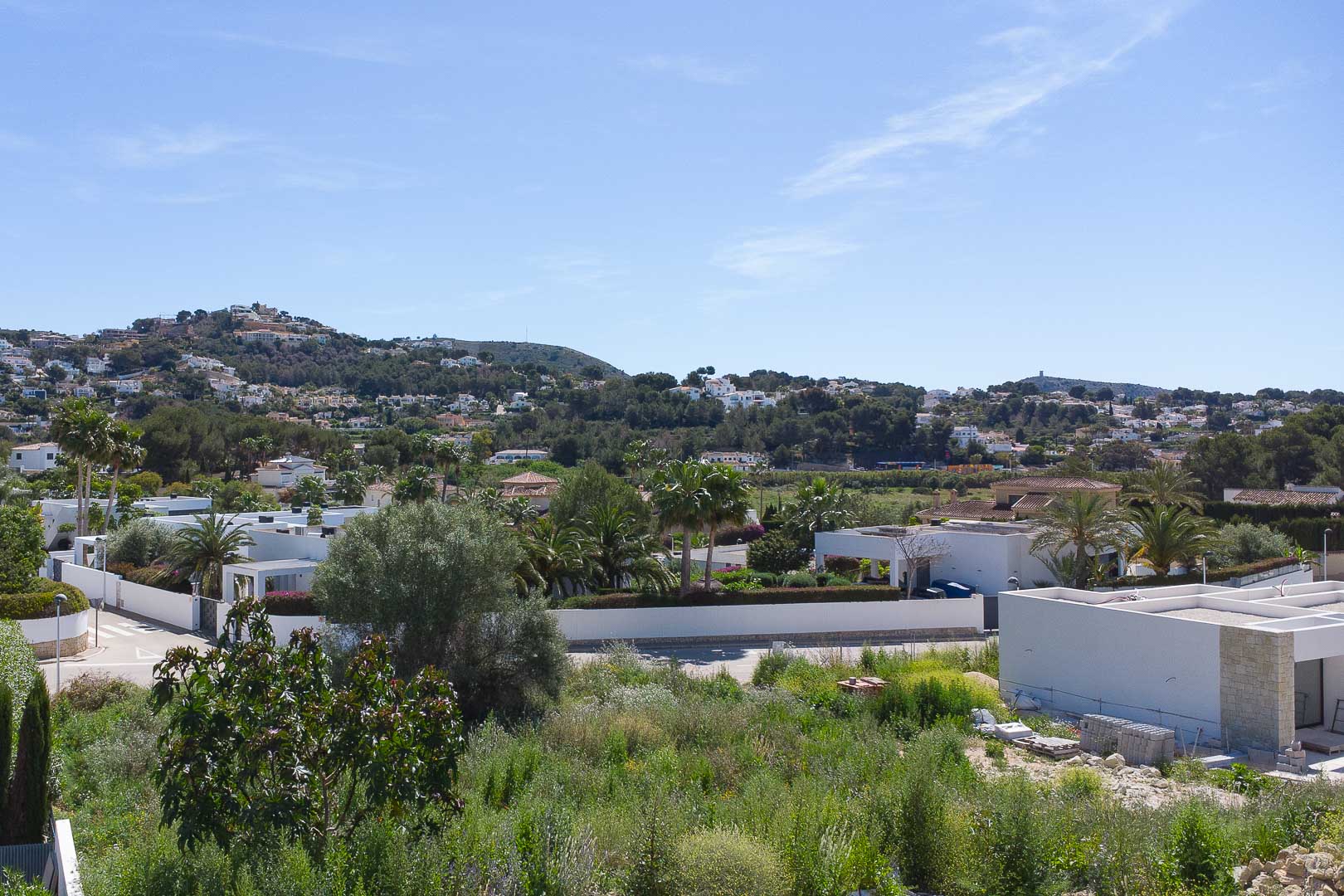 Verhoogd panoramisch uitzicht over de woonwijk van Moraira, met moderne witte villa's omgeven door mediterrane vegetatie en glooiende heuvels.