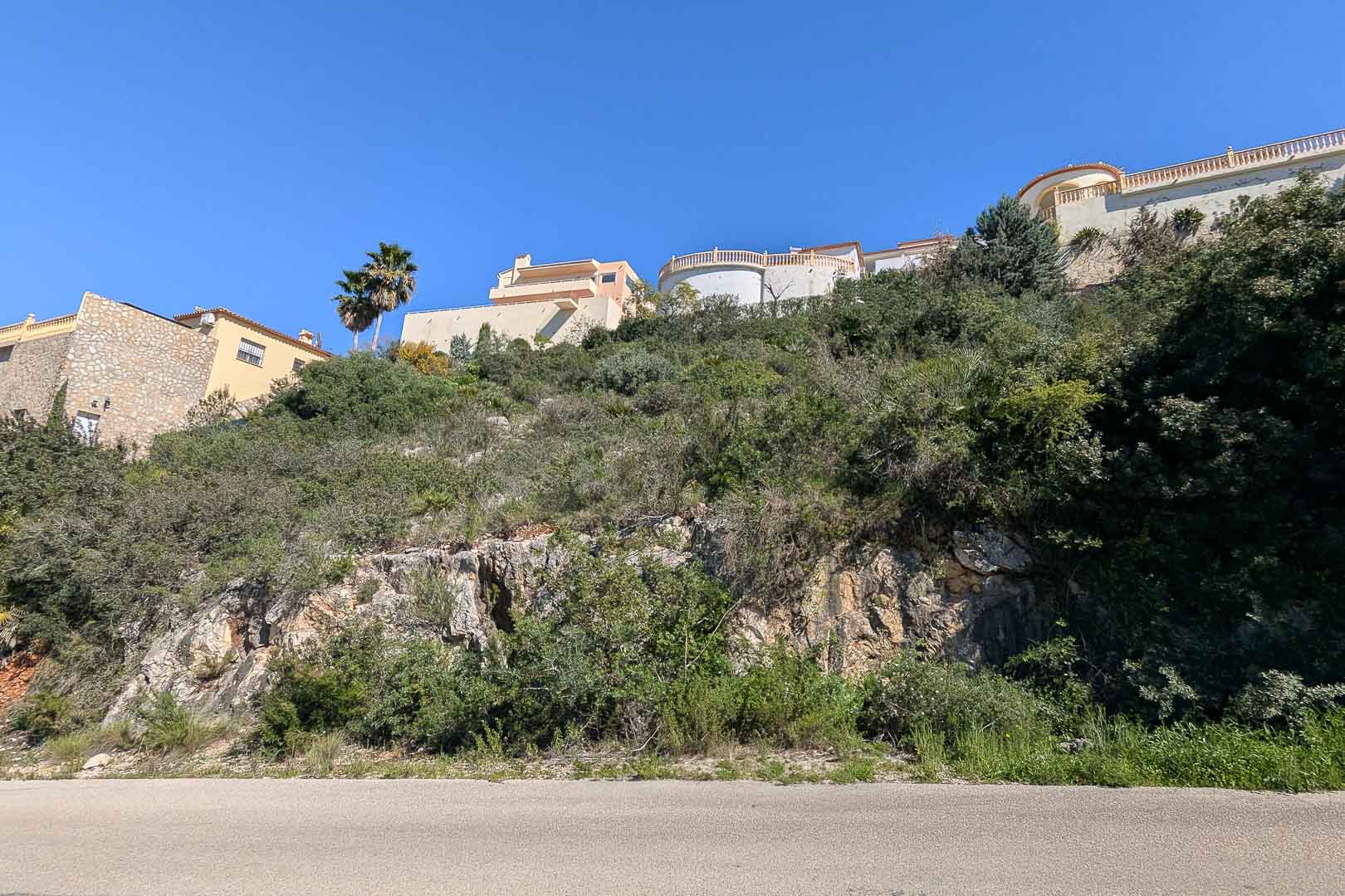 Buitenaanzicht van een villa in aanbouw in Pedreguer, Costa Blanca, omgeven door mediterrane vegetatie en natuurlijke rotsen.