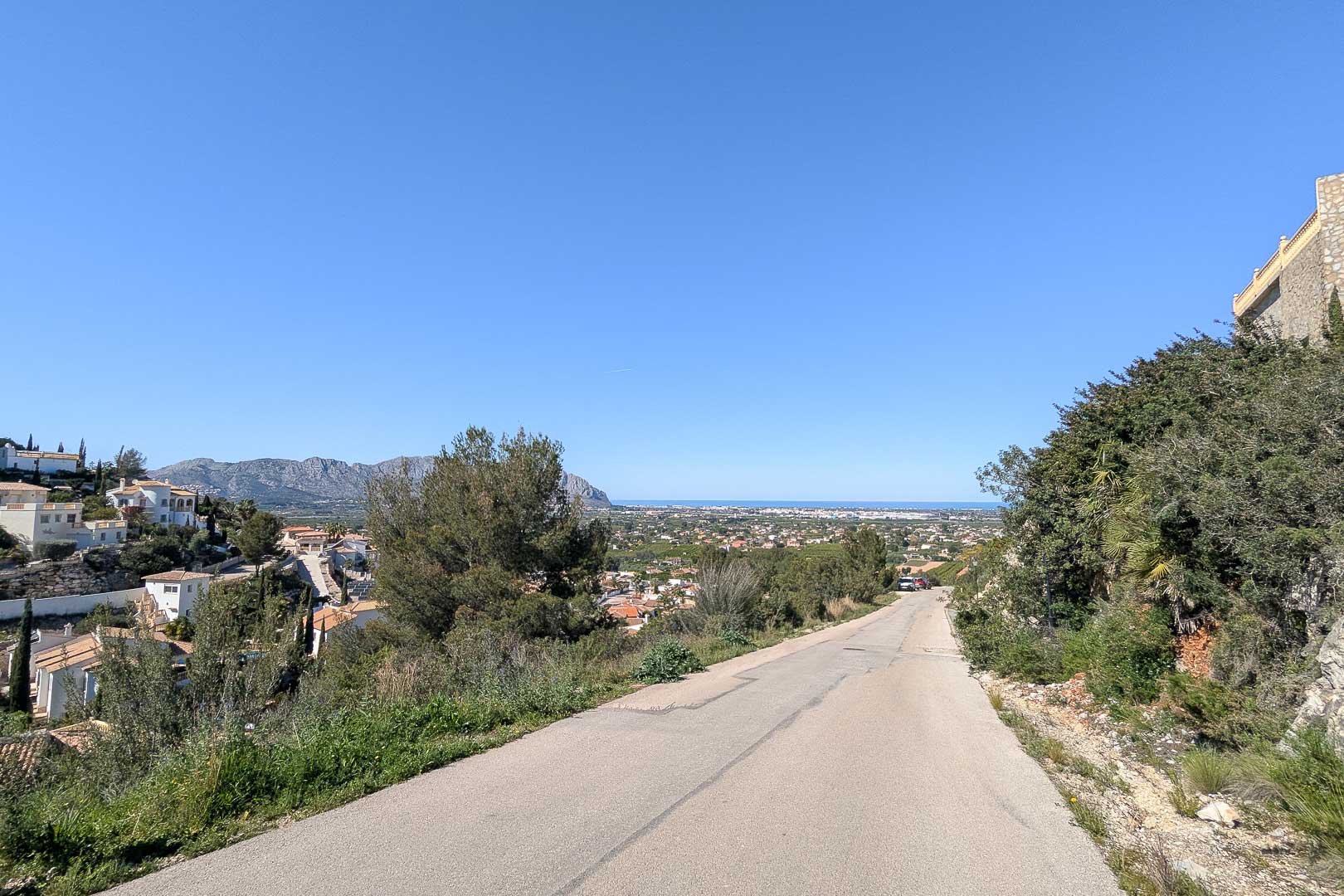 Toegangsweg tot de villa met panoramisch uitzicht op Pedreguer en de Middellandse Zee aan de horizon onder een heldere hemel.
