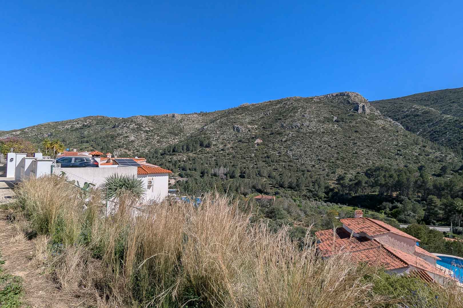 Panoramisch uitzicht op de bergen en de vallei vanaf het perceel, met het natuurlijke mediterrane landschap en de omliggende villa's.