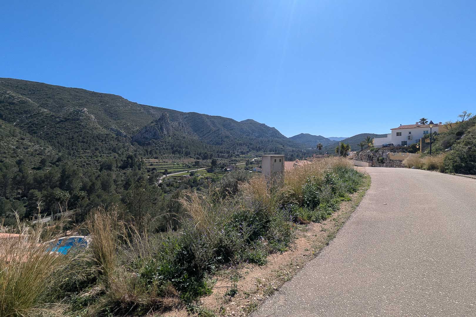 Panoramisch uitzicht vanaf de toegangsweg op de vallei en de omliggende bergen van Pedreguer onder een heldere, blauwe hemel.