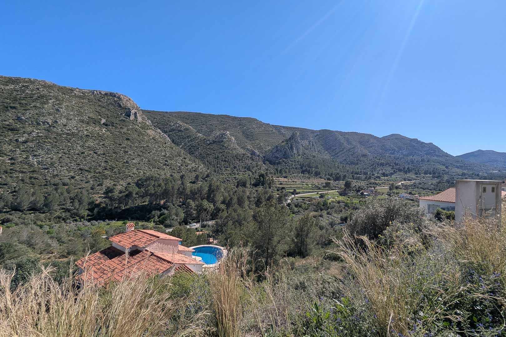 Verhoogd panoramisch uitzicht over de vallei en de bergen van Pedreguer, met mediterrane begroeiing en een nabijgelegen villa met zwembad.