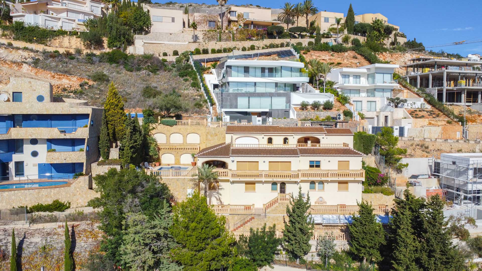Exterieur van de traditionele villa in La Corona, met een crèmekleurige gevel, terracotta daken en gelaagde terrassen met balustrades gebouwd tegen de steile helling.