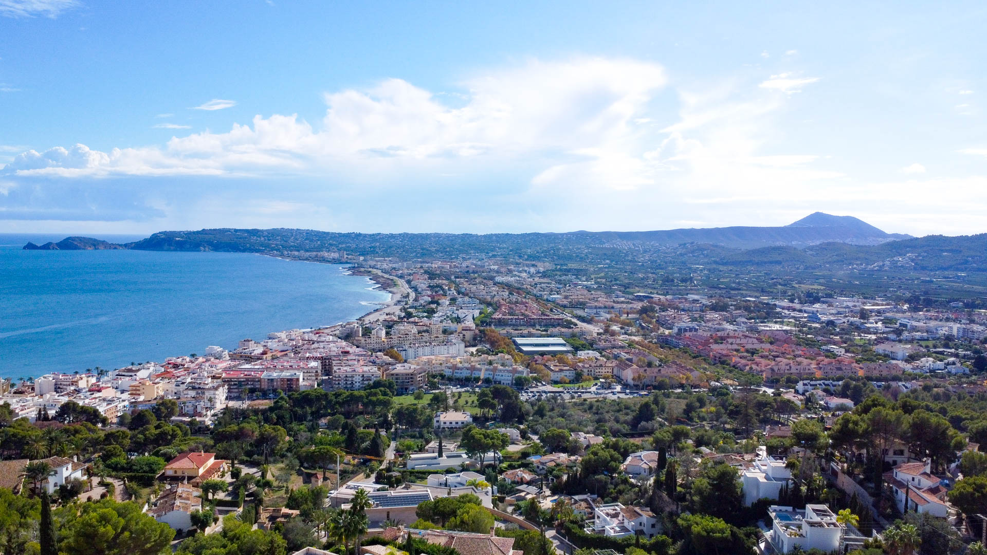 Panoramisch luchtfoto van de baai van Jávea, met de Middellandse Zeekust, het stadscentrum en het omliggende berglandschap bij helder daglicht.